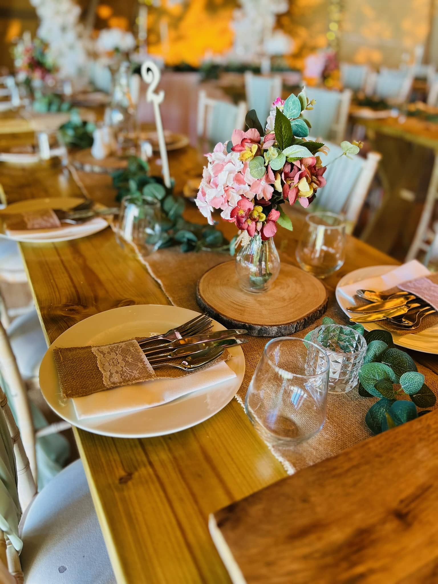 Elegant table setting with floral centerpiece, wooden accents, and rustic decor in a warmly lit event space.