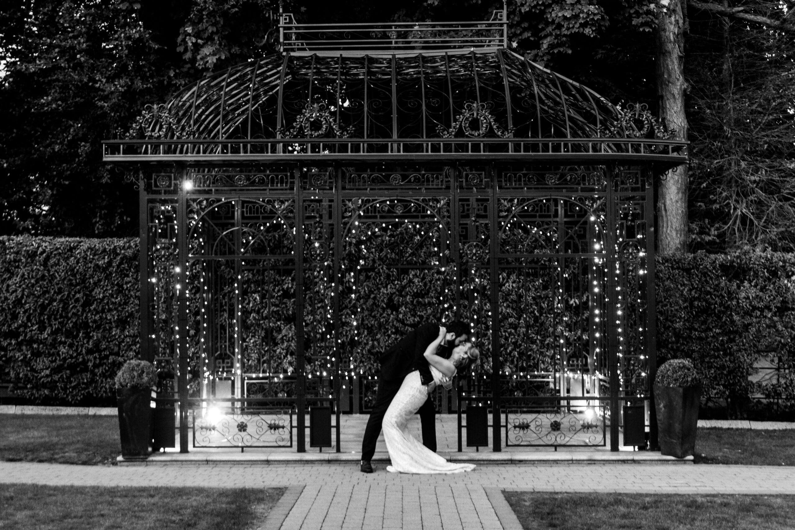 Couple dancing romantically in front of an ornate gazebo with twinkling lights at night.