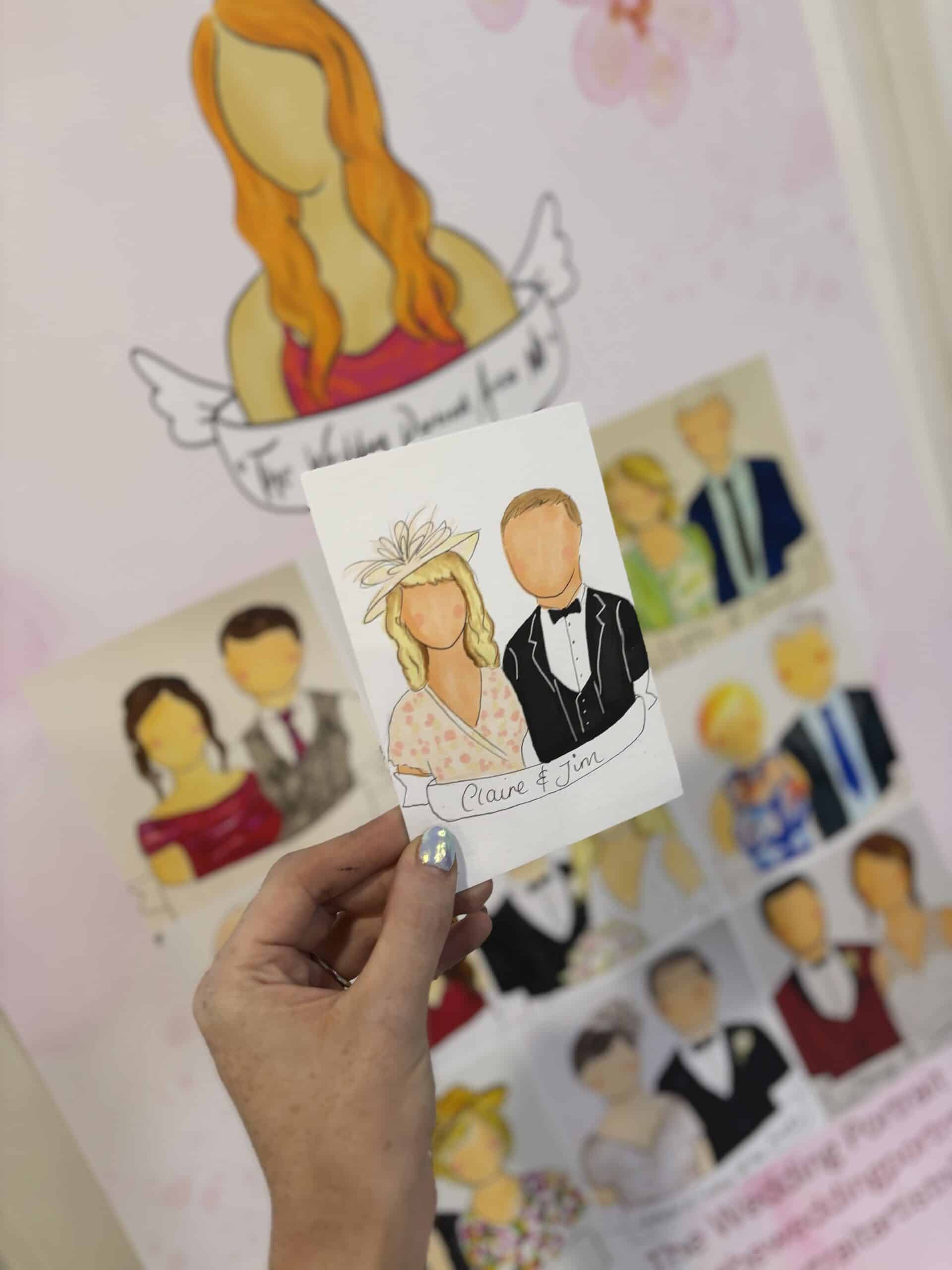 Hand holding a cartoon-style wedding portrait of a couple, with similar artworks visible in the background.