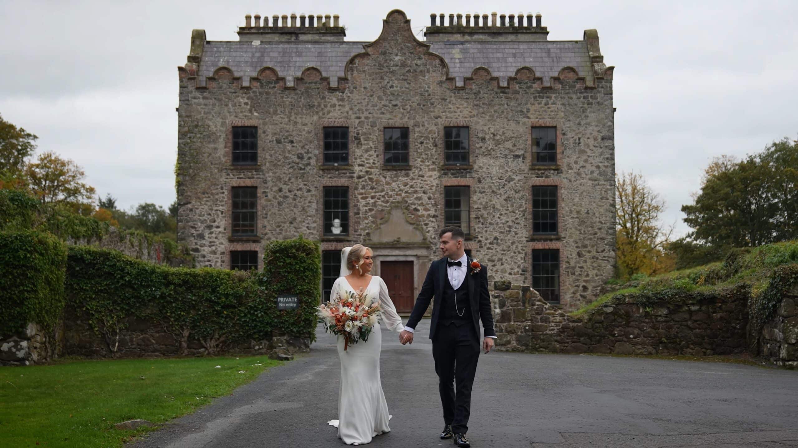 Bride and groom holding hands outside a historic stone building.