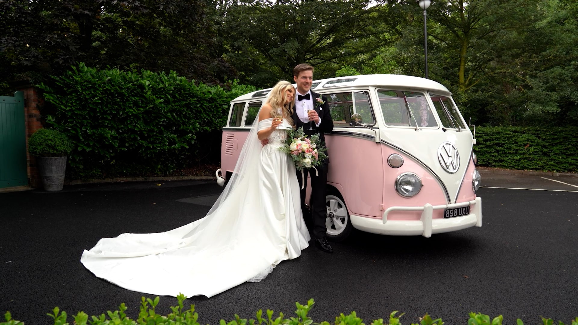 Bride and groom celebrate with champagne beside a vintage pink VW bus.