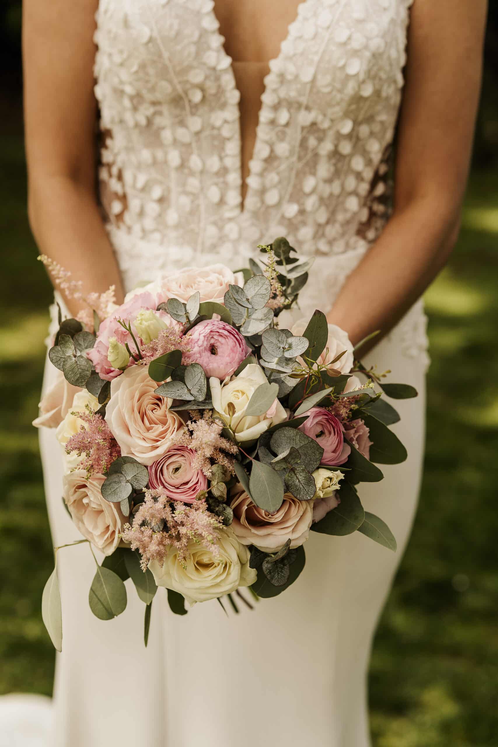 Bride holding a bouquet of pink and white roses with greenery.