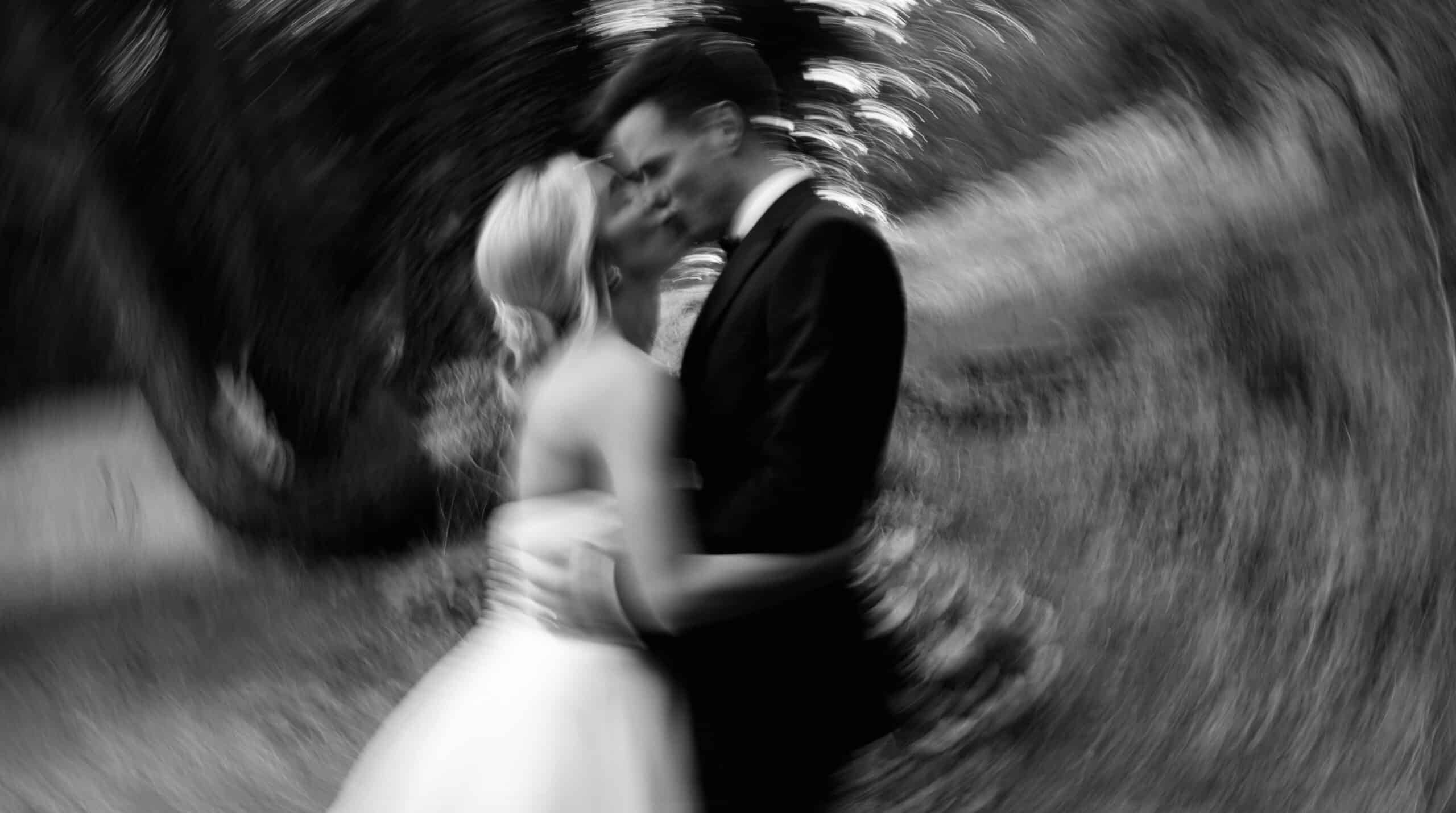 Blurred black and white image of a couple kissing outdoors.