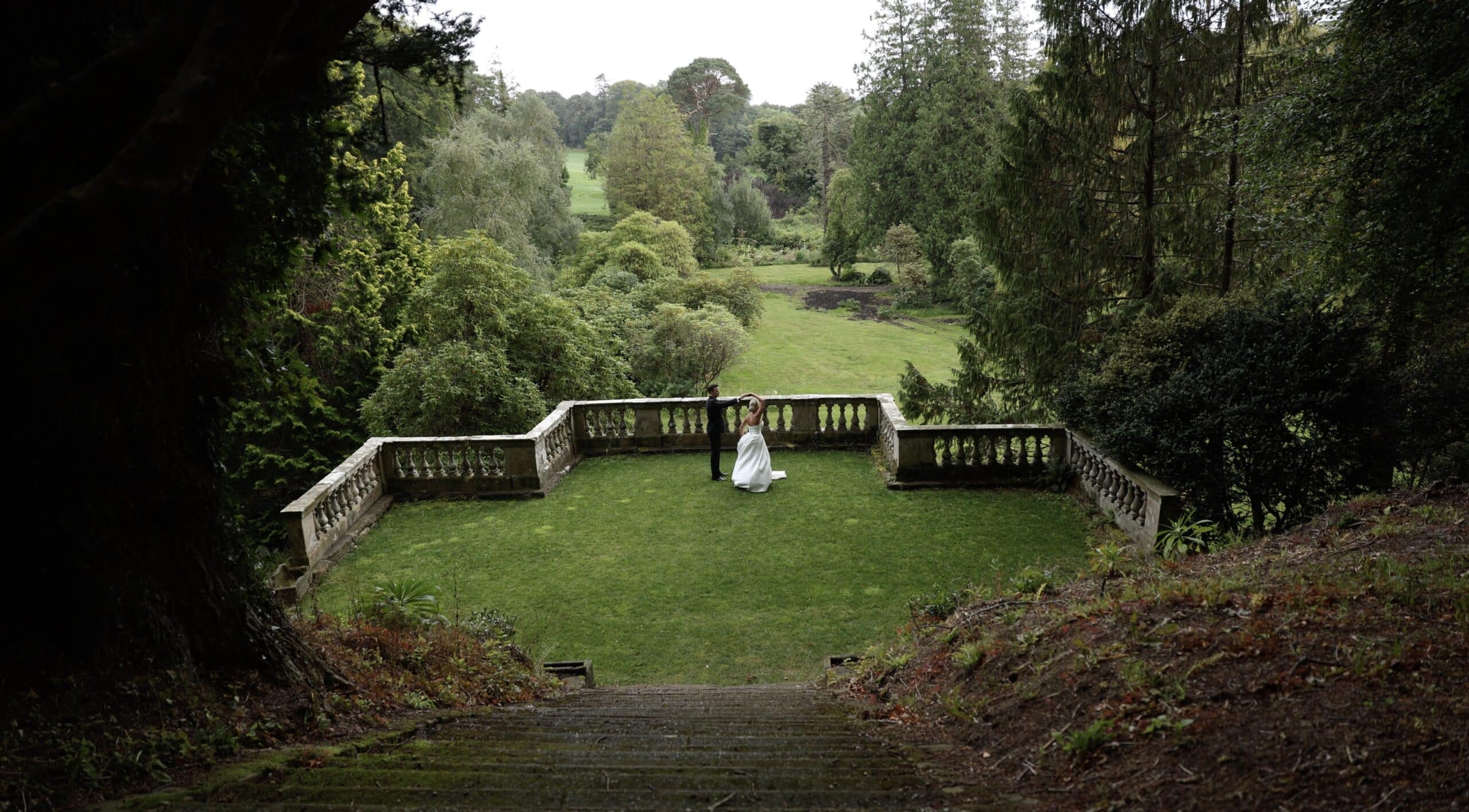 Bride and groom dancing on a terrace surrounded by lush greenery.