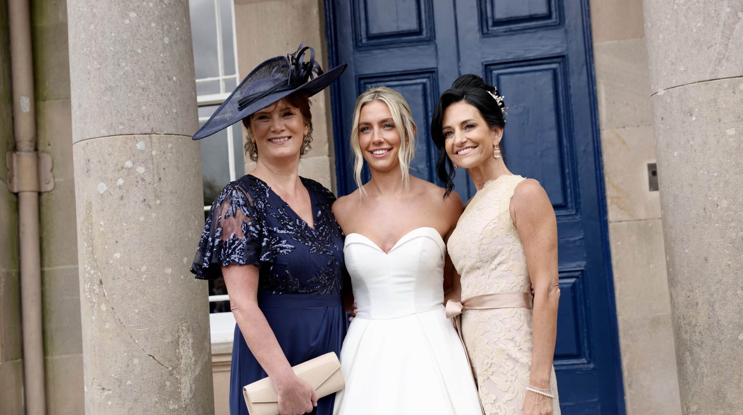 Three women dressed elegantly, posing in front of a blue door.