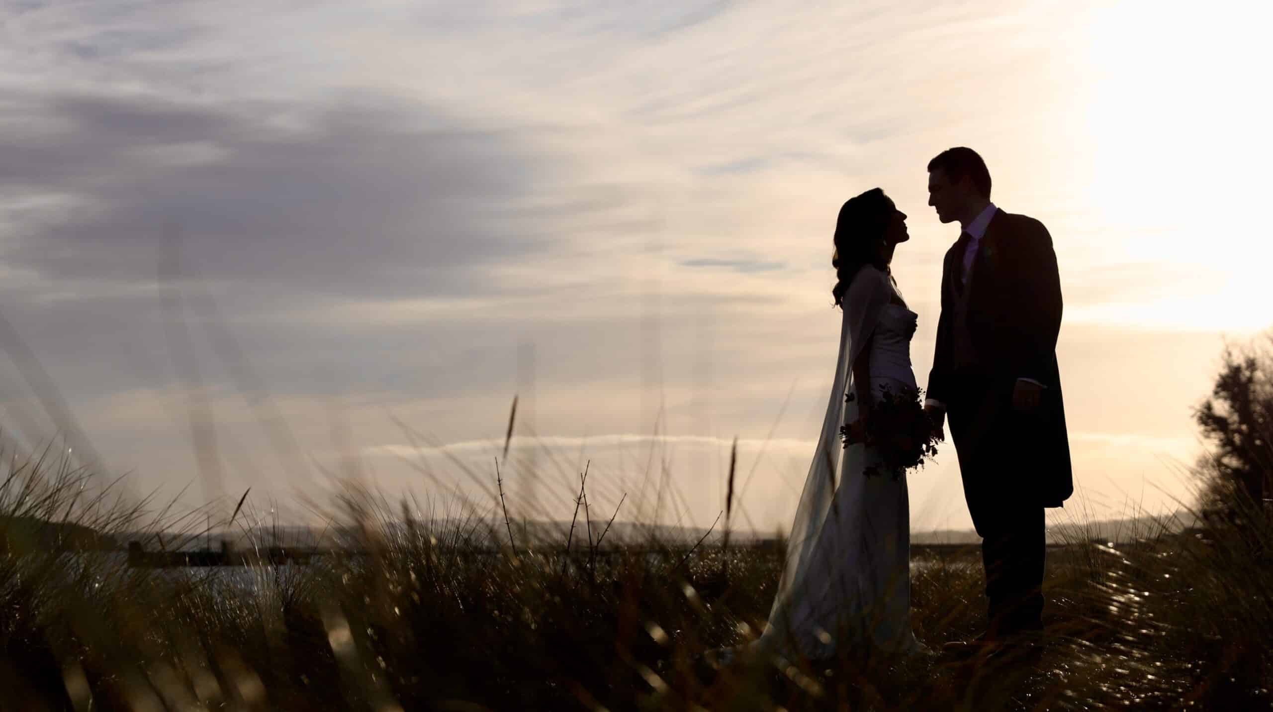 Silhouetted couple standing in a grassy field at sunset.