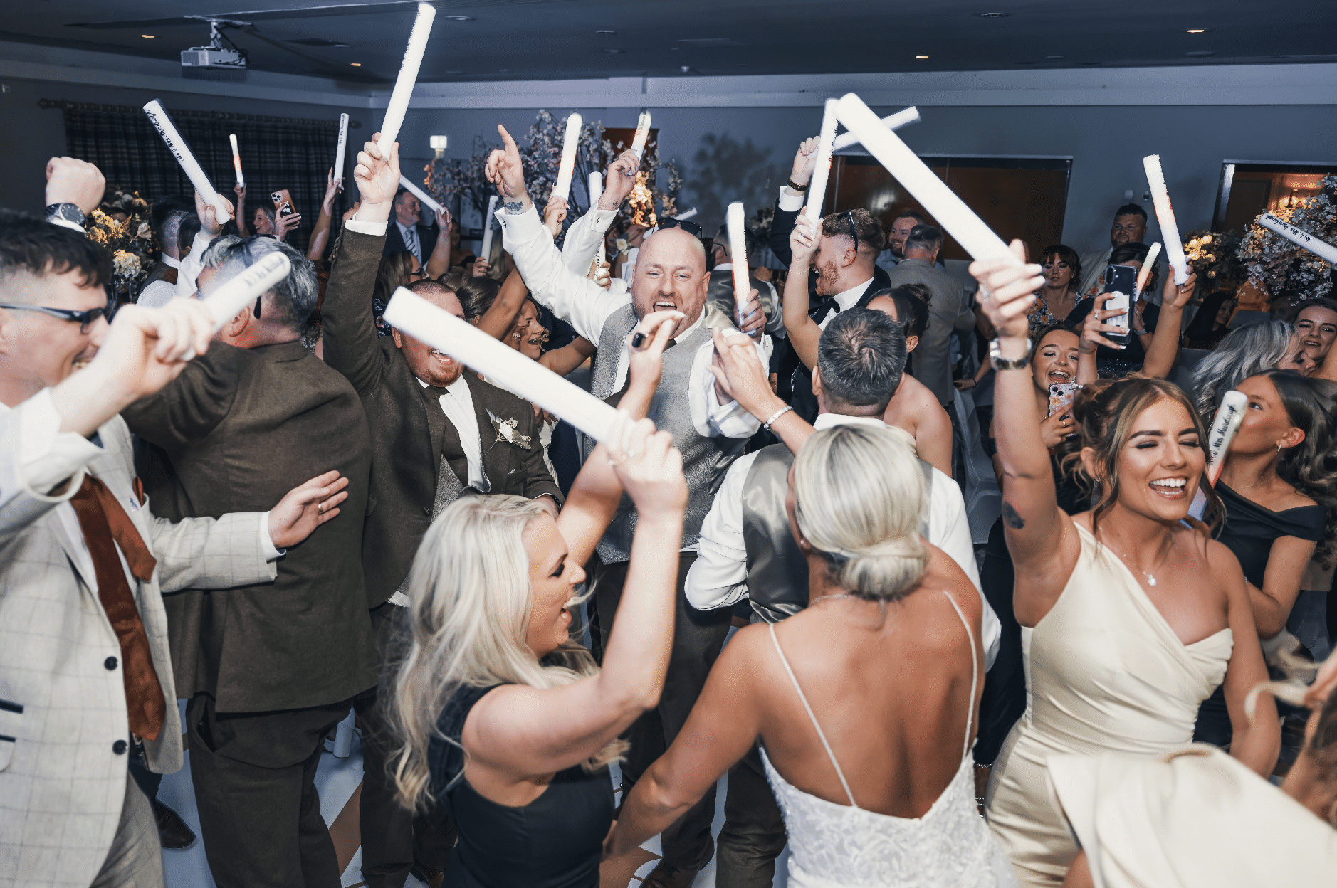 People celebrating at a lively party with glow sticks raised in excitement.