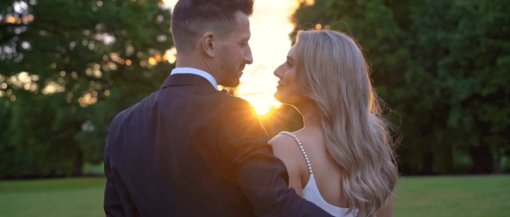 Couple in formal attire gazing at each other with sunset in the background.