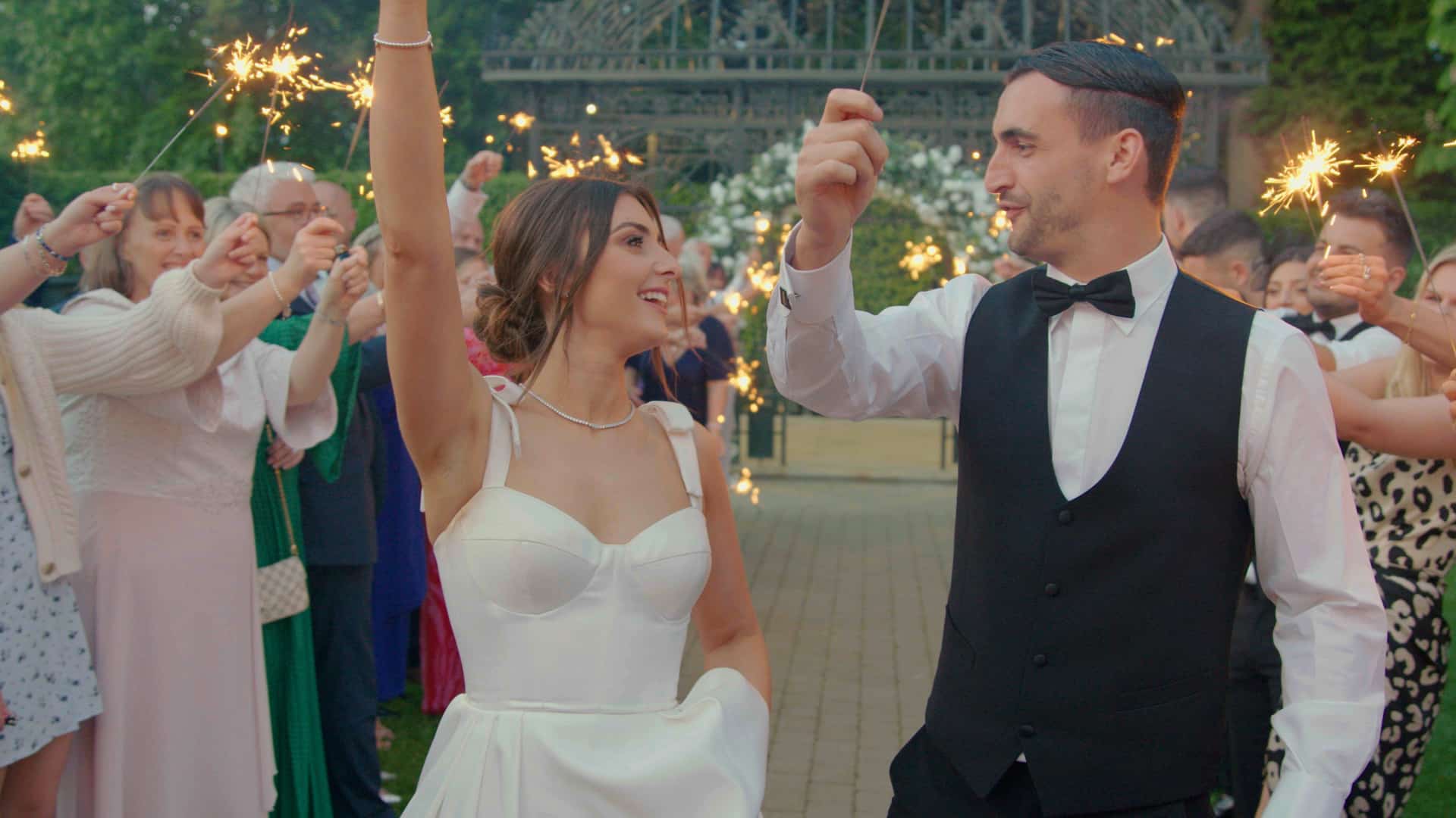 Bride and groom holding sparklers surrounded by guests celebrating.