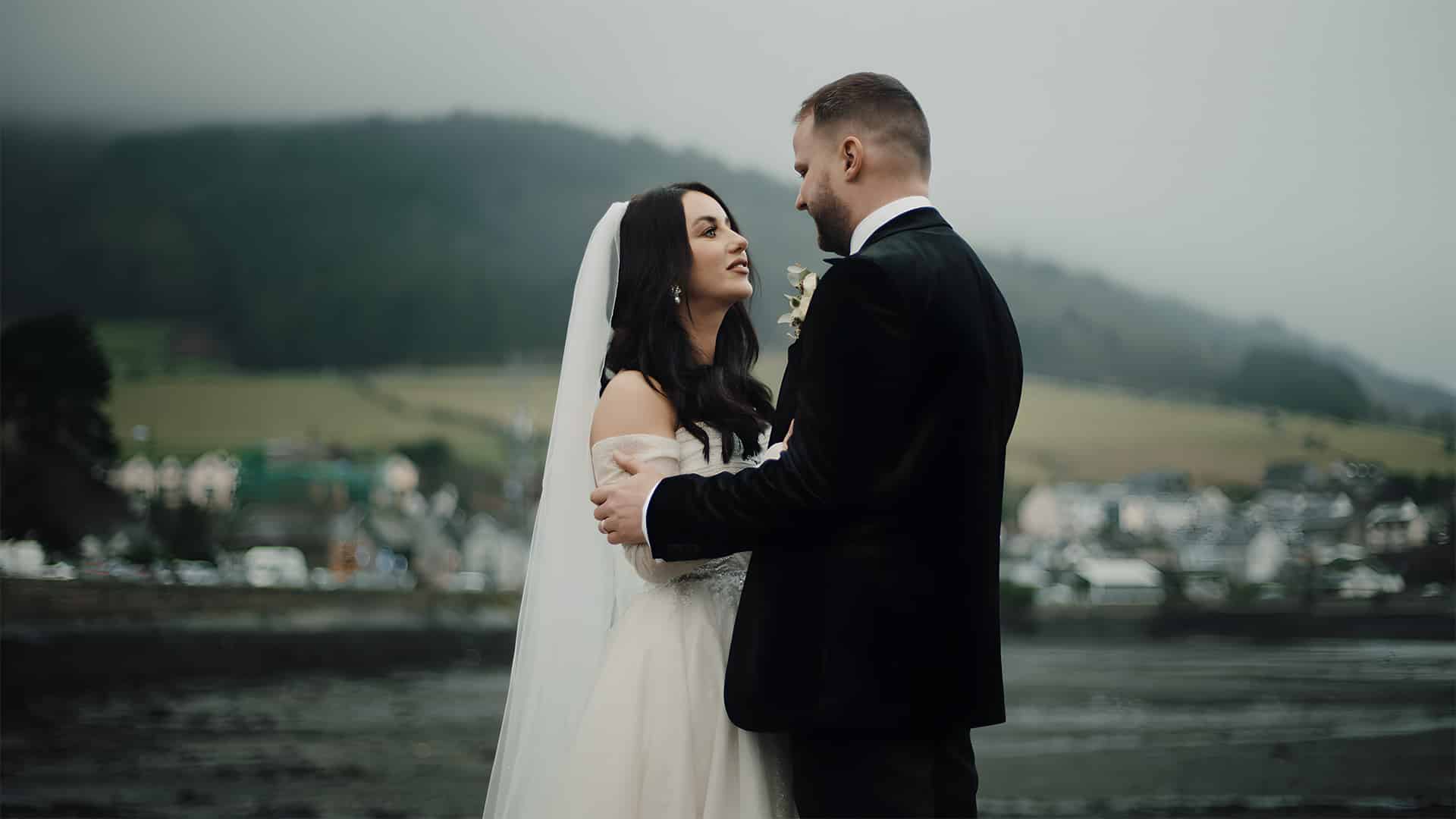 Bride and groom embracing outdoors with a scenic landscape background.