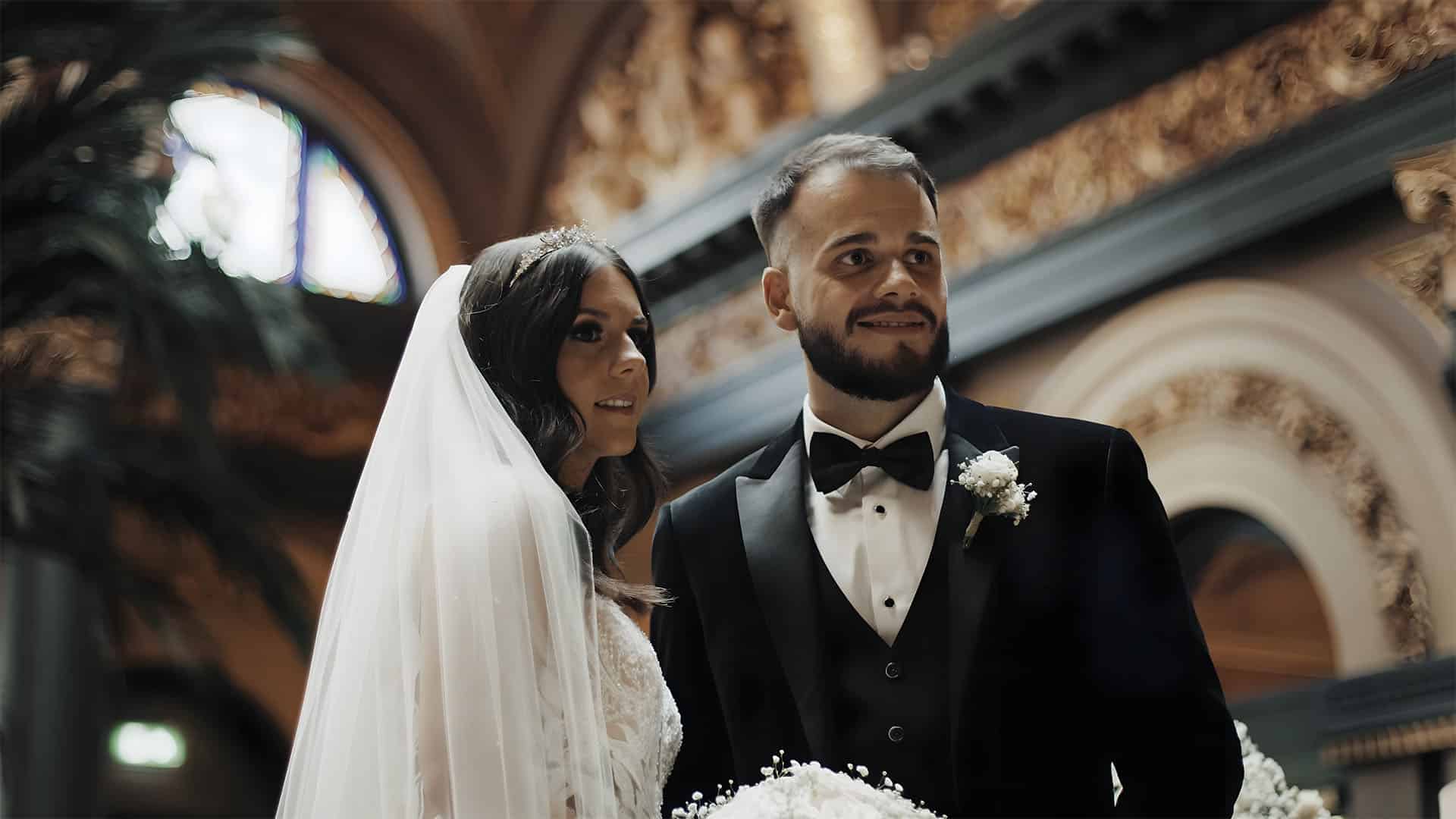 Bride and groom in elegant attire standing in a beautifully decorated venue.