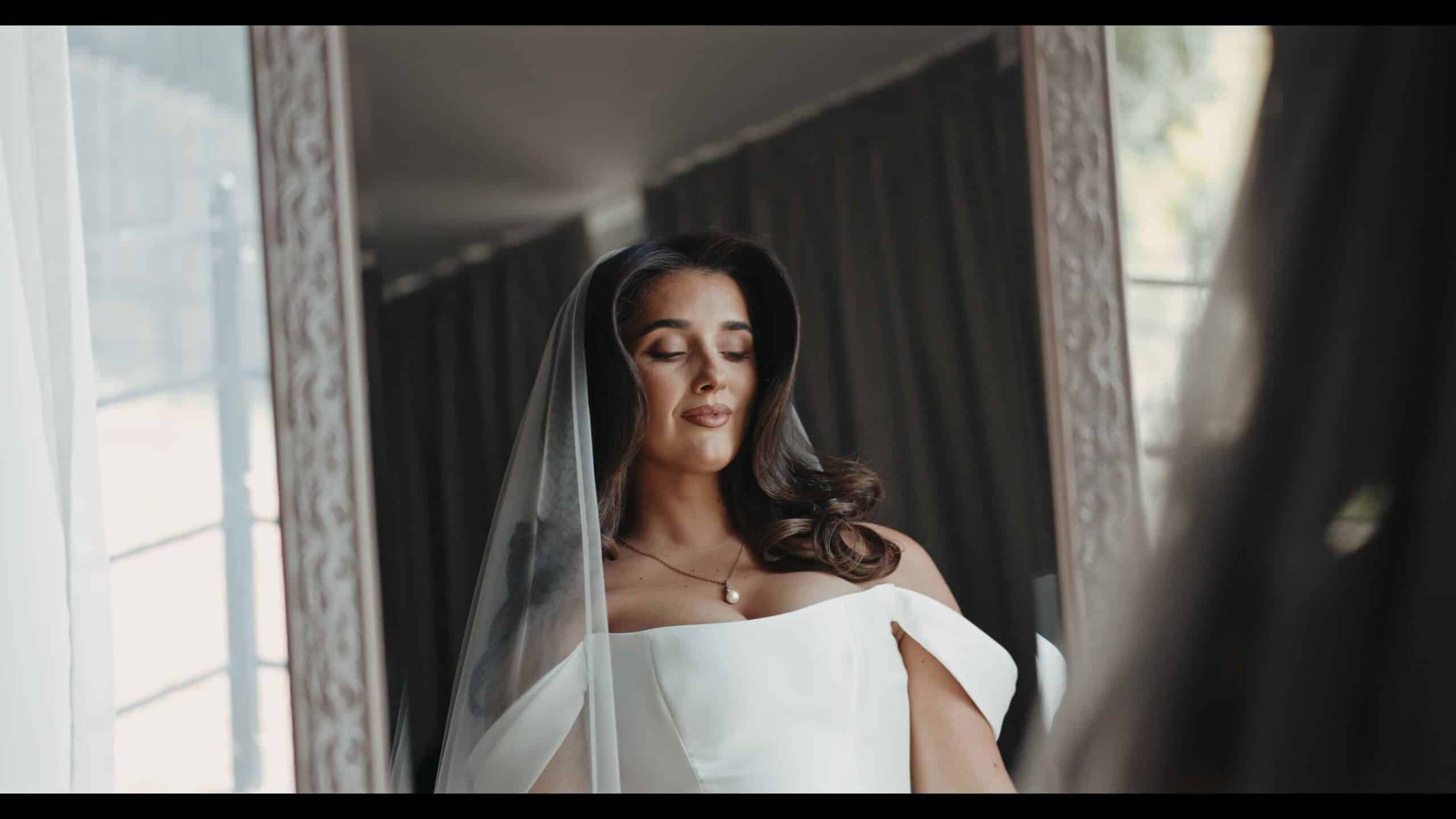 Bride in elegant white dress and veil, reflecting dreamily in mirror.