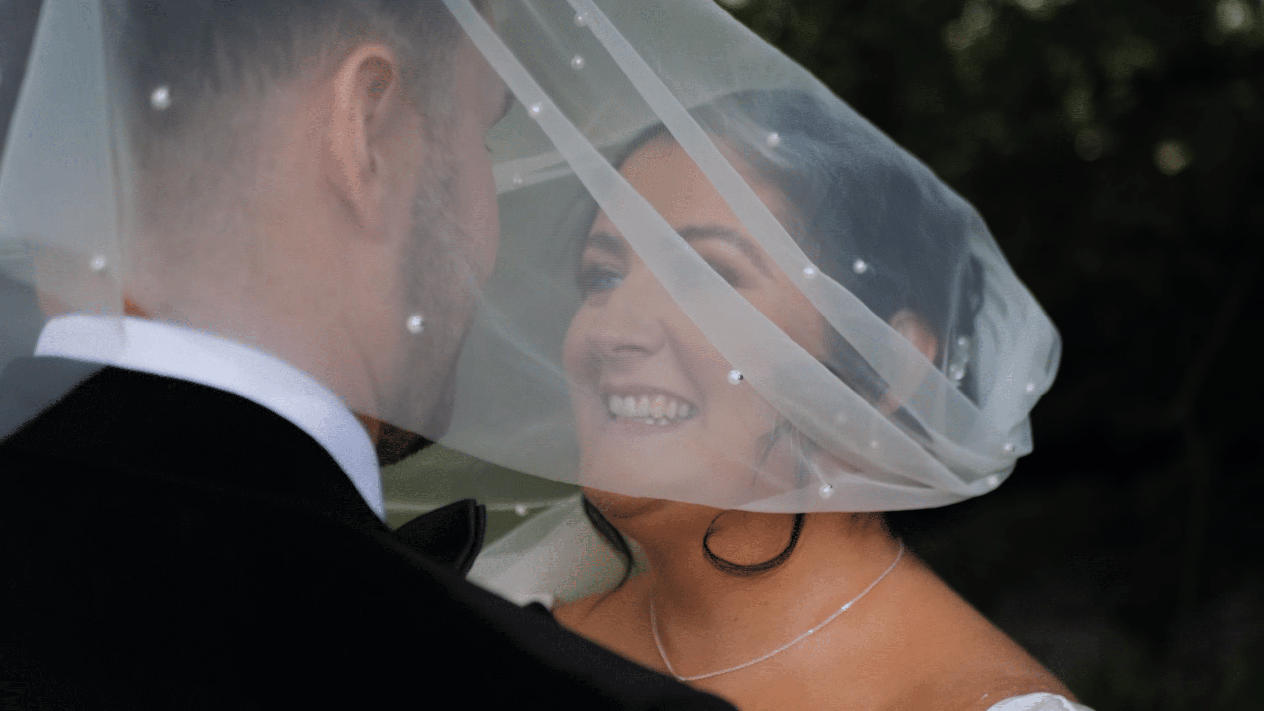 Bride and groom smiling under a wedding veil, close-up.