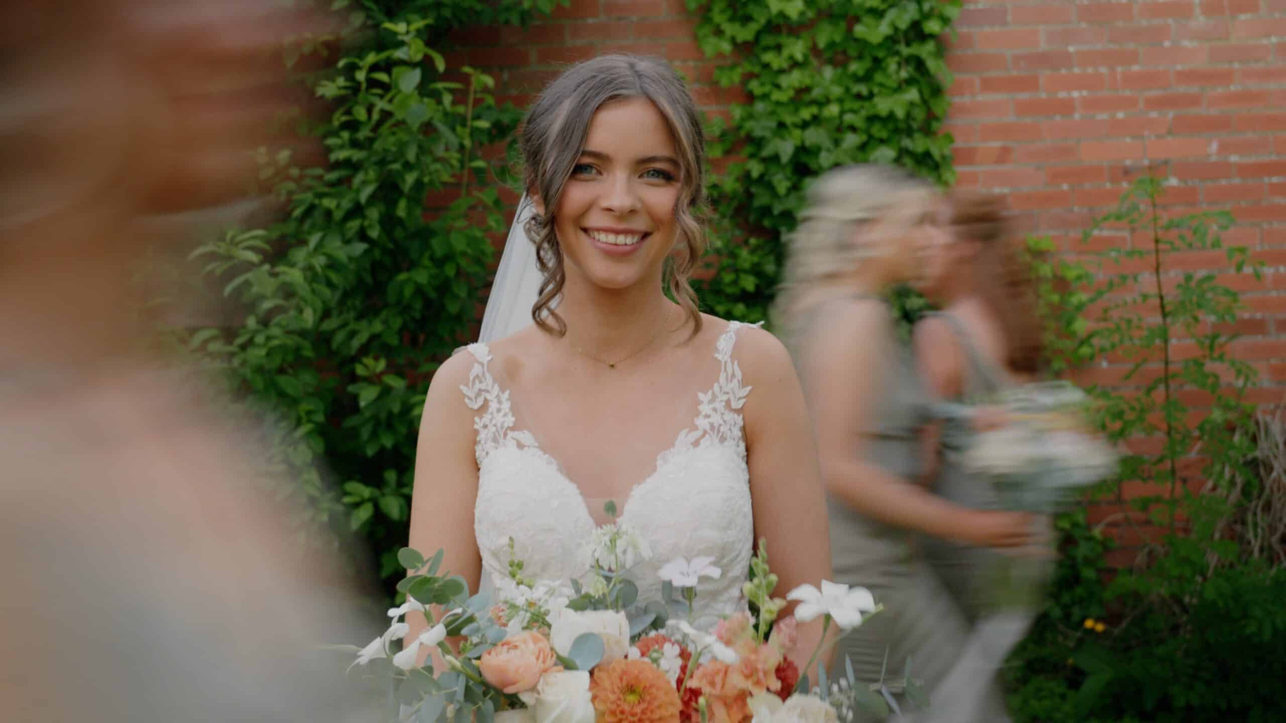 Bride smiling, holding a bouquet in front of a brick wall covered with ivy.