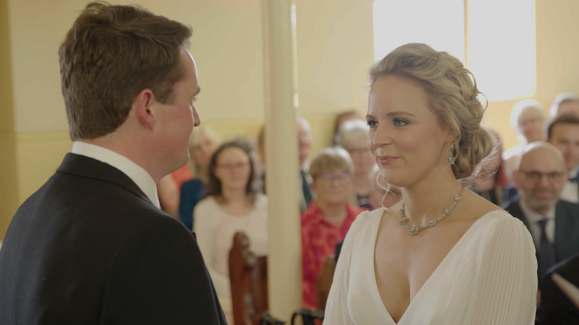 Bride and groom facing each other during a wedding ceremony, with guests in the background.