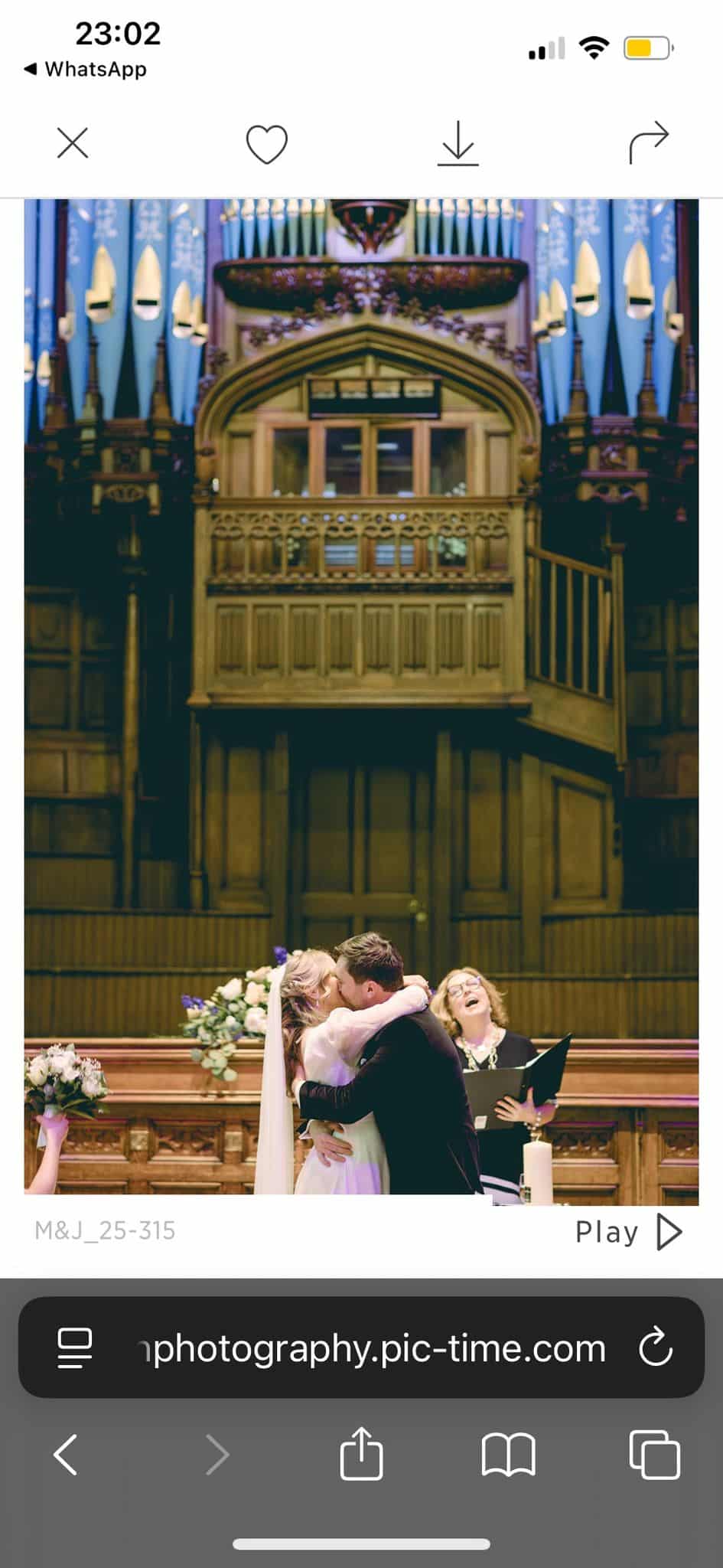 Bride and groom kissing at a wedding ceremony in a church, with an officiant smiling in the background.