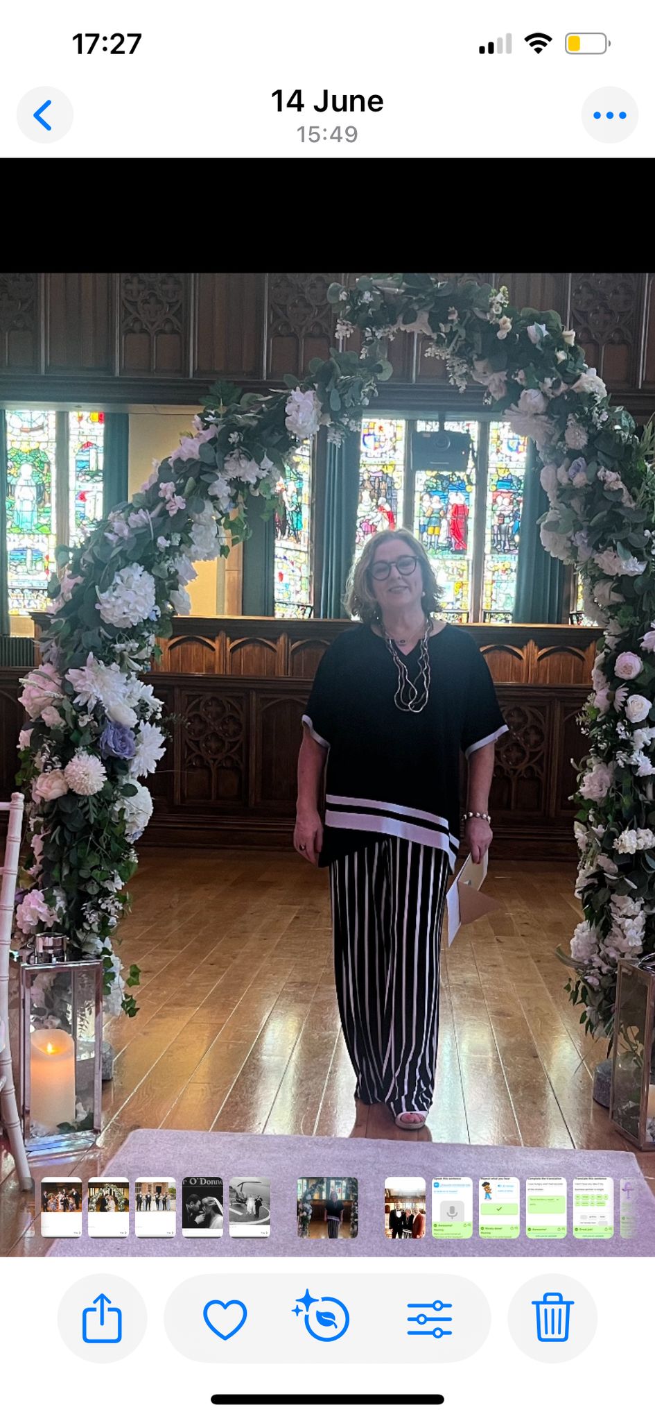 Woman standing under floral arch in a church with stained glass windows.