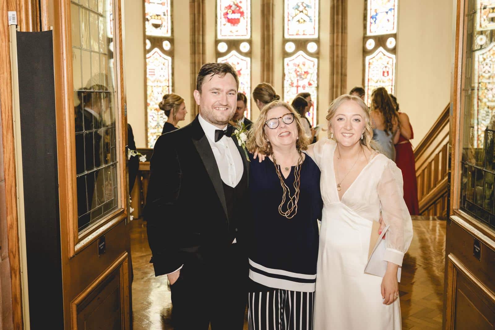 Three people smiling indoors, with stained glass windows in the background.