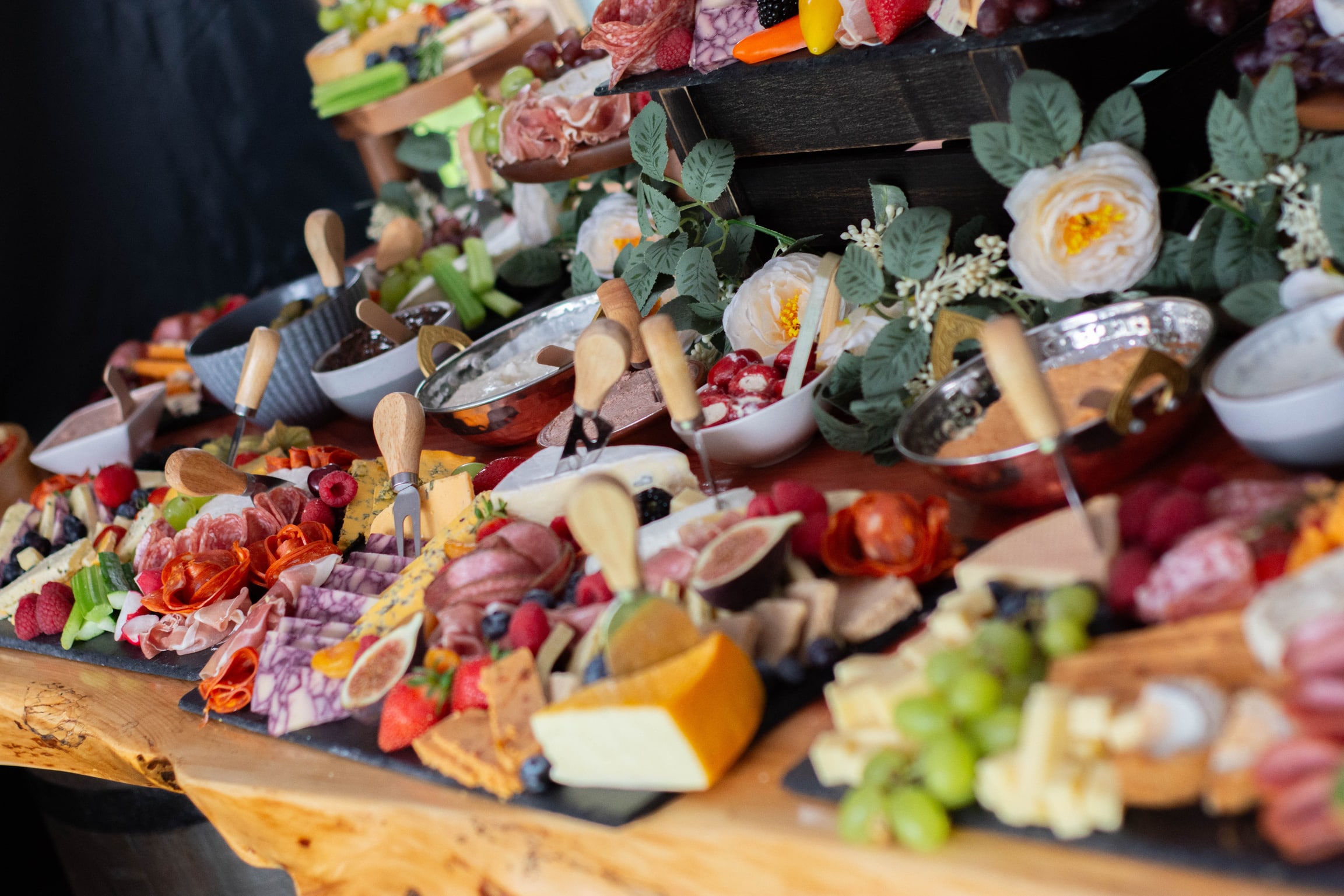 Assorted charcuterie board with meats, cheeses, fruits, and floral decorations.