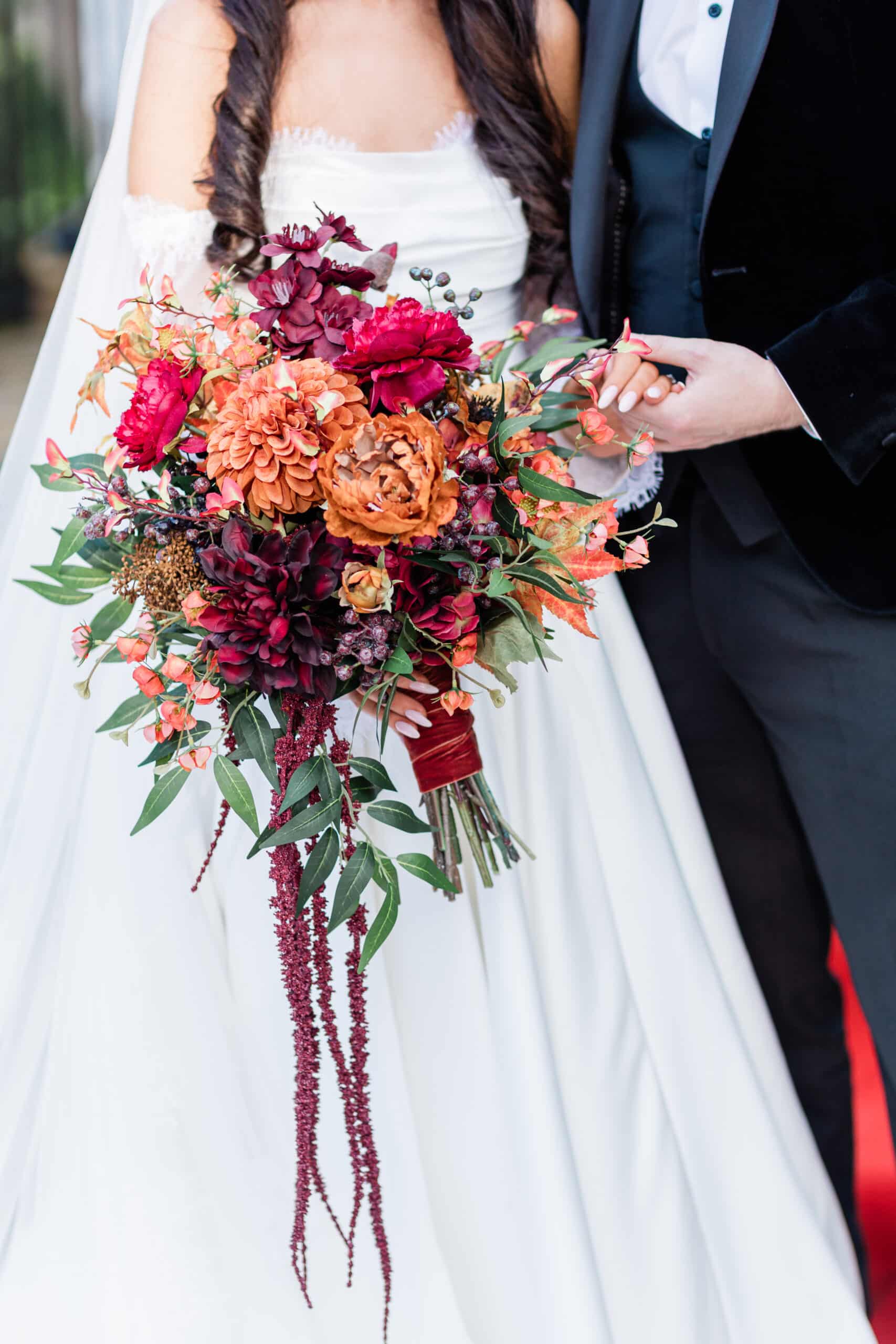 Bride holding a vibrant bouquet with red and orange flowers, standing beside the groom in formal attire.