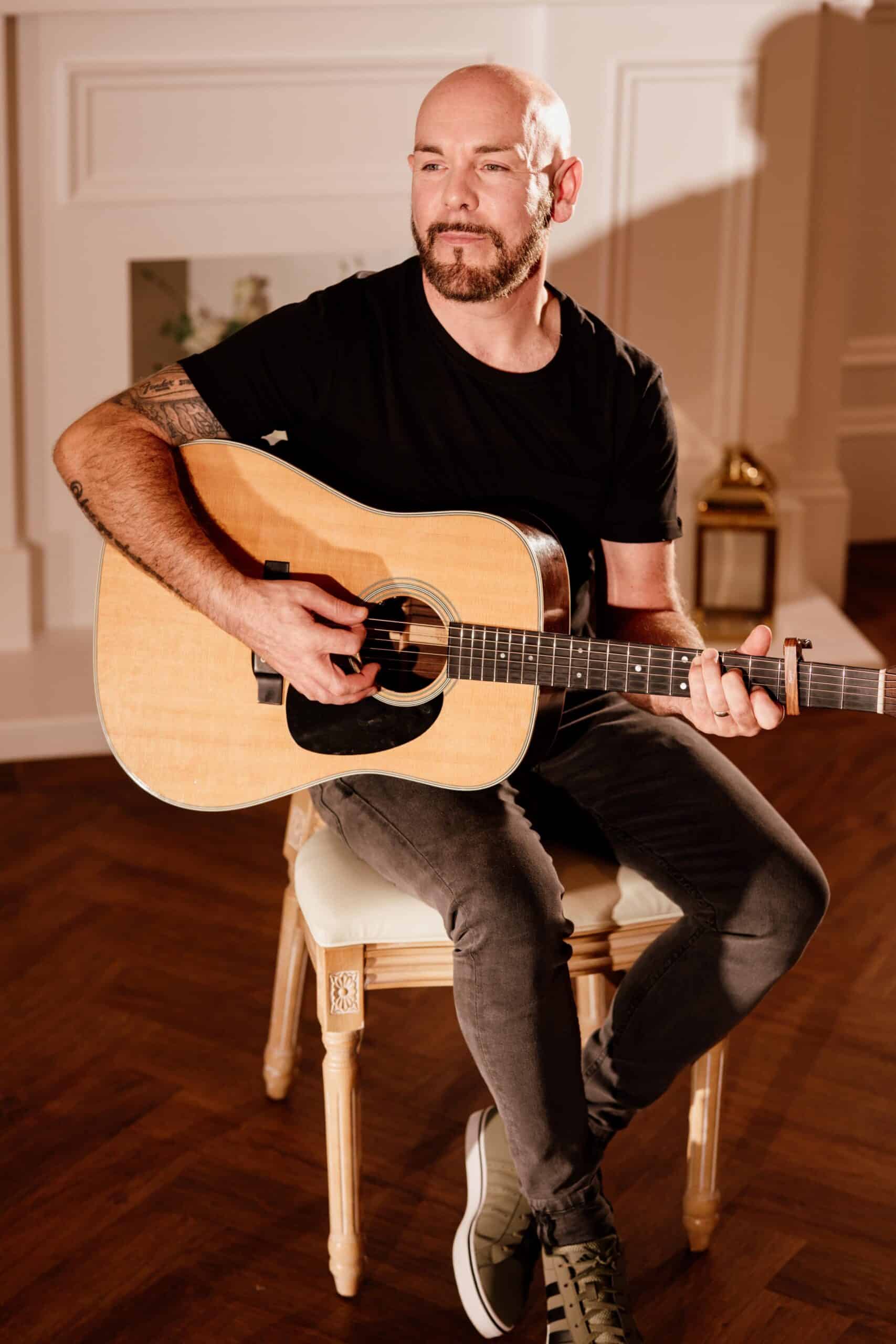 Man sitting and playing an acoustic guitar indoors.