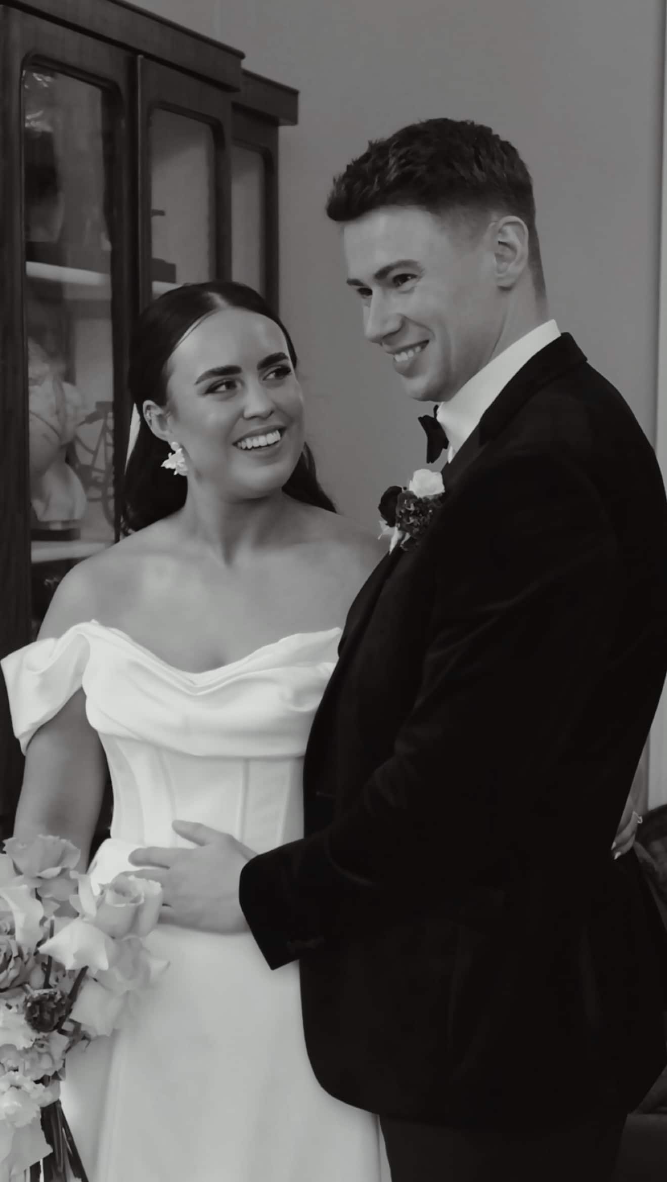 Bride and groom smiling at each other, dressed in wedding attire.