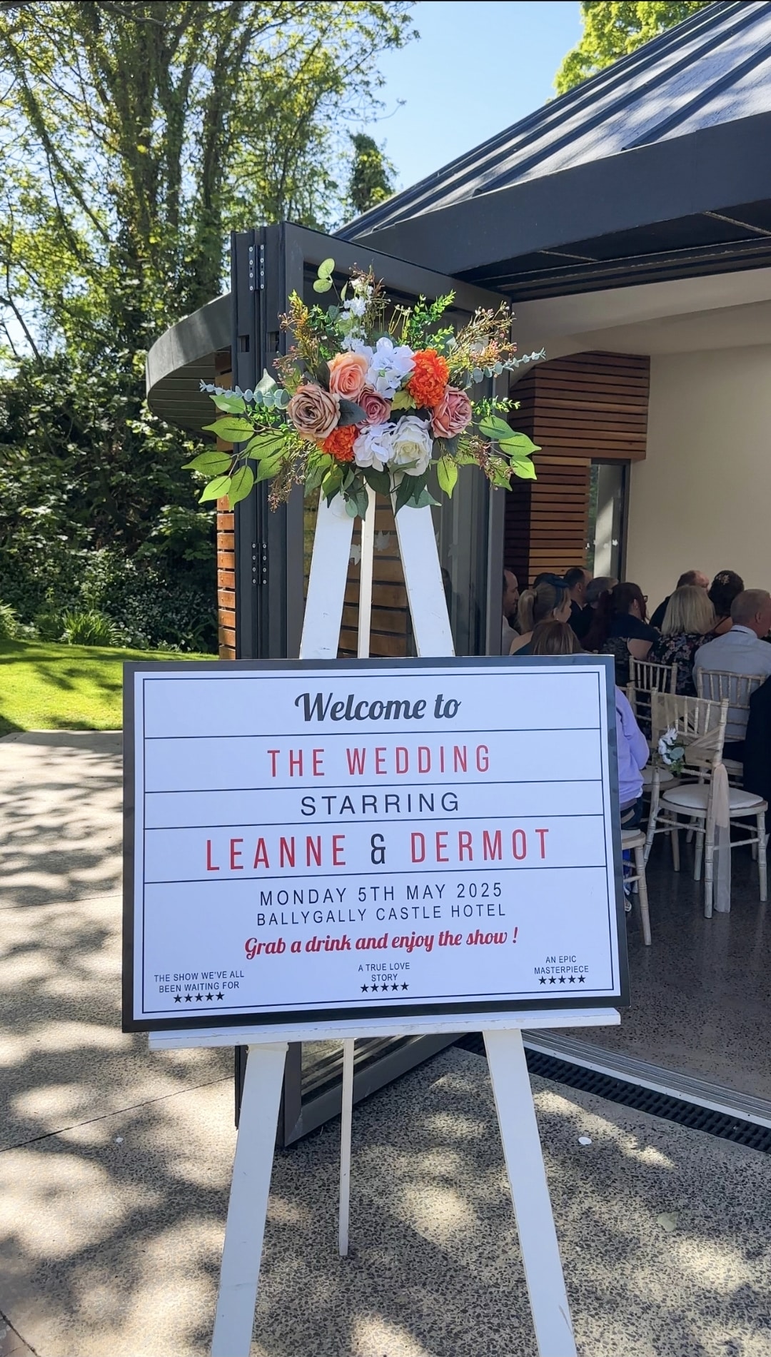 Wedding welcome sign with floral arrangement at Ballygally Castle Hotel entrance.