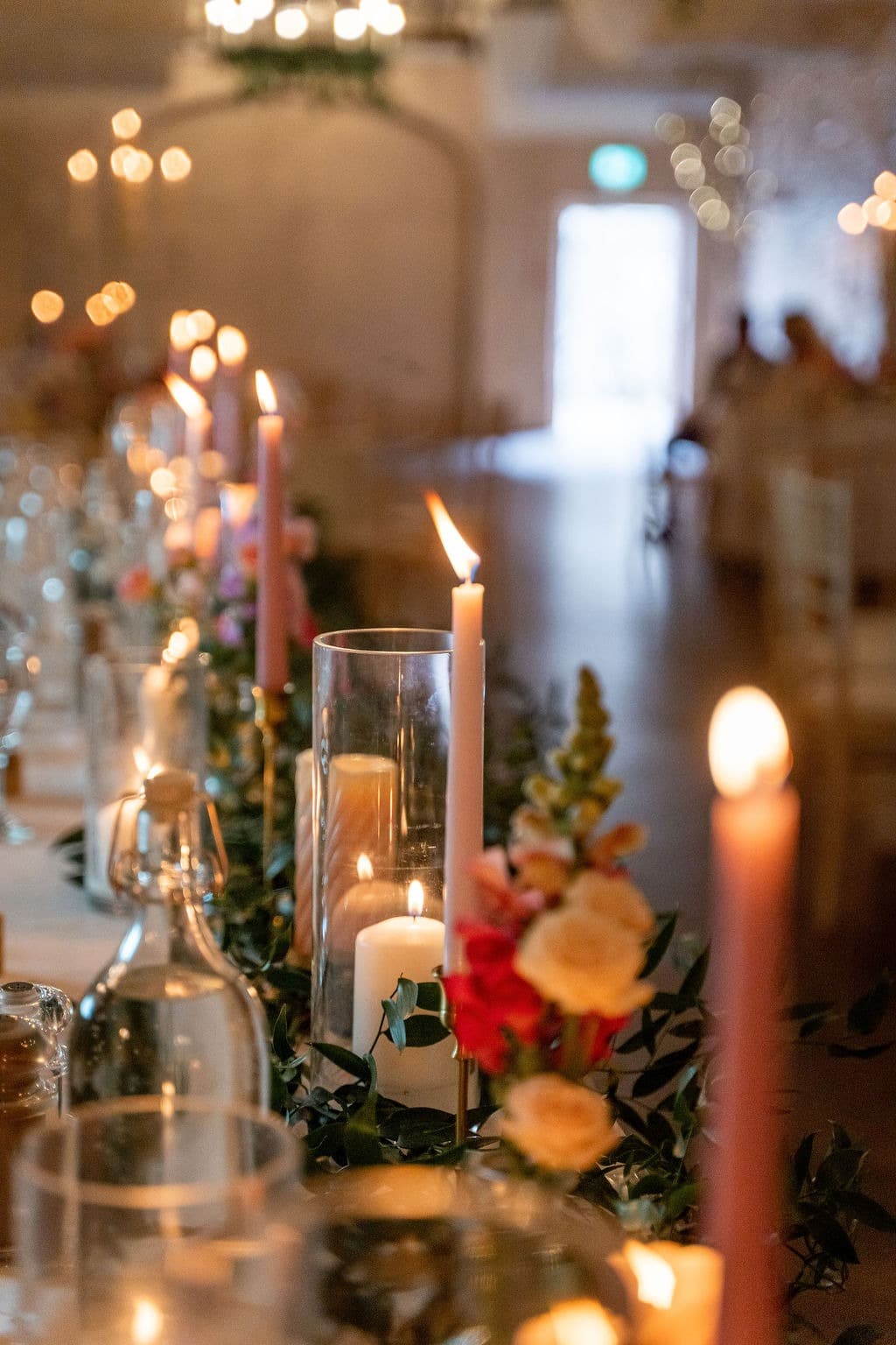 Elegant table setting with lit candles and floral arrangements in a softly lit room.