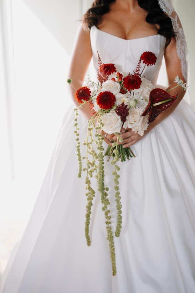 Bride holding a bouquet of red and white flowers in a white wedding dress.