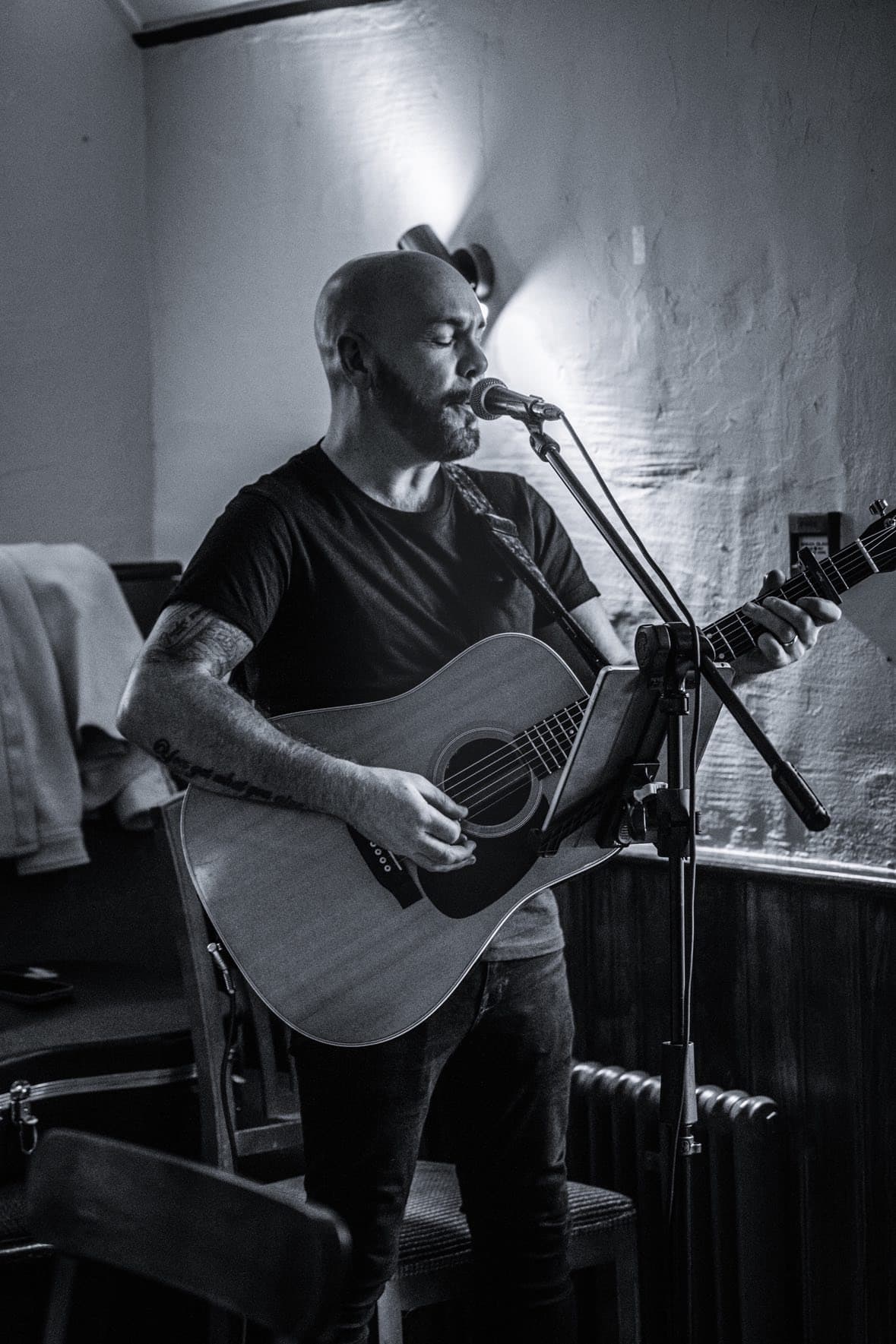 Musician playing guitar and singing into a microphone in a dimly lit room.