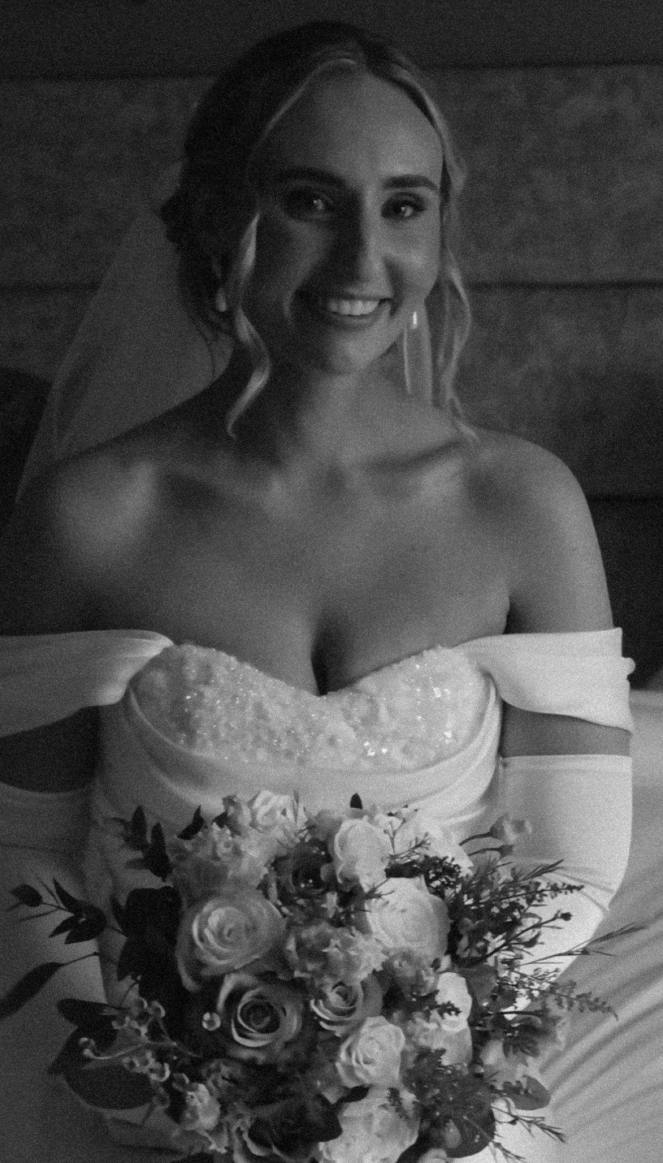 Bride smiling, holding a bouquet of roses, in black and white portrait.