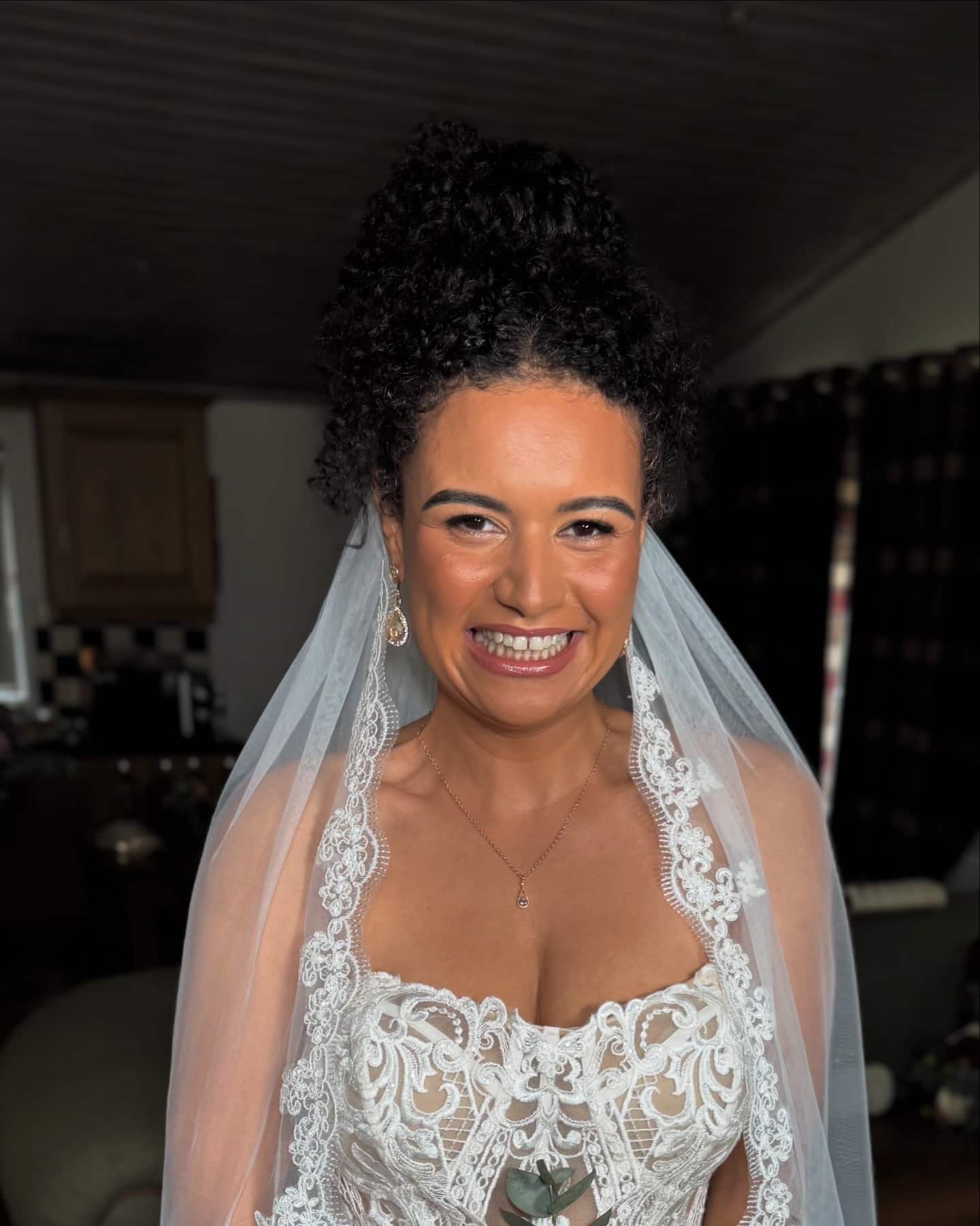Bride in lace wedding dress and veil smiling indoors.