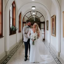 Bride and groom standing in an elegant hallway, embracing and smiling.