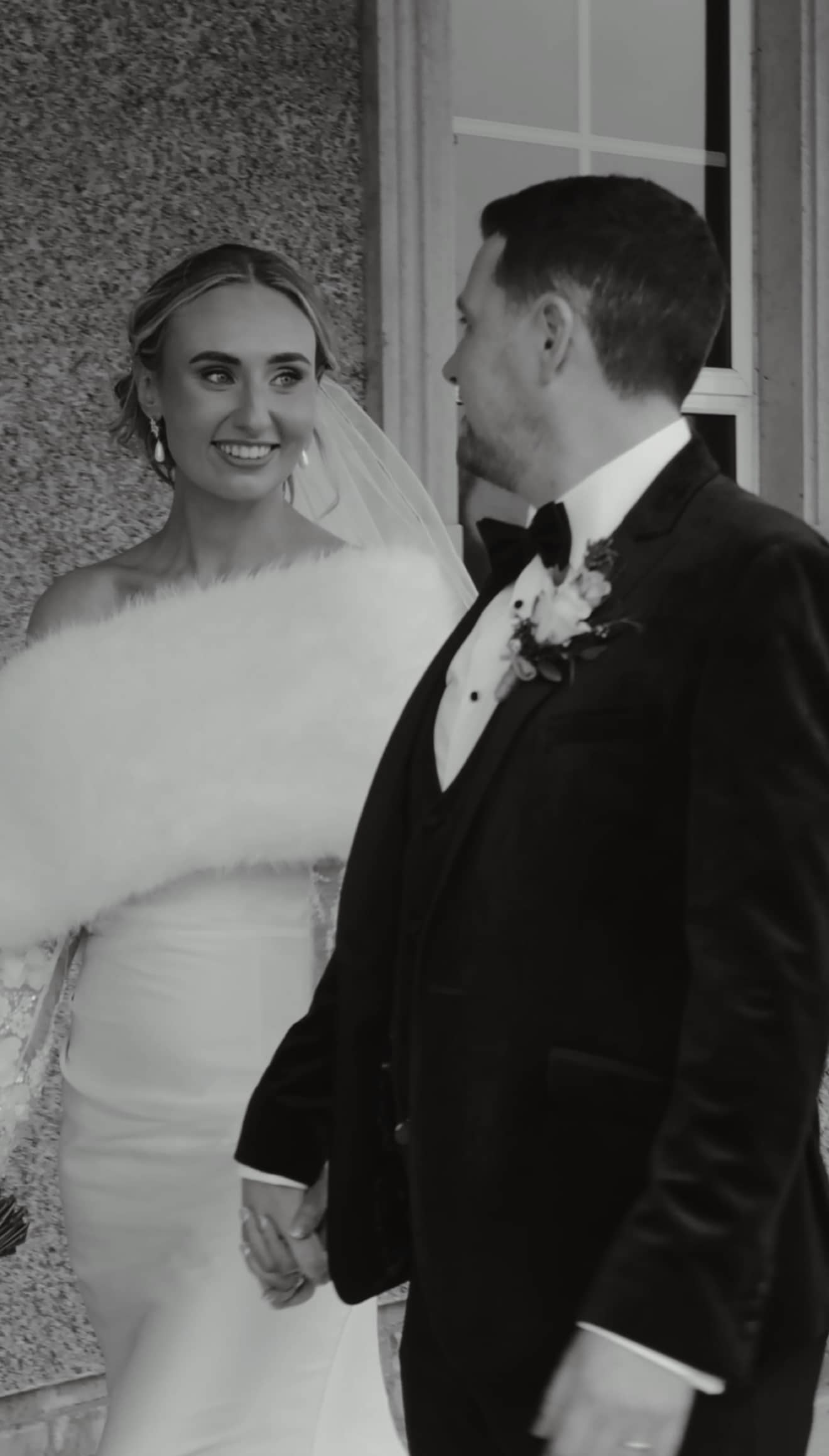 Bride and groom smiling and holding hands in elegant wedding attire.