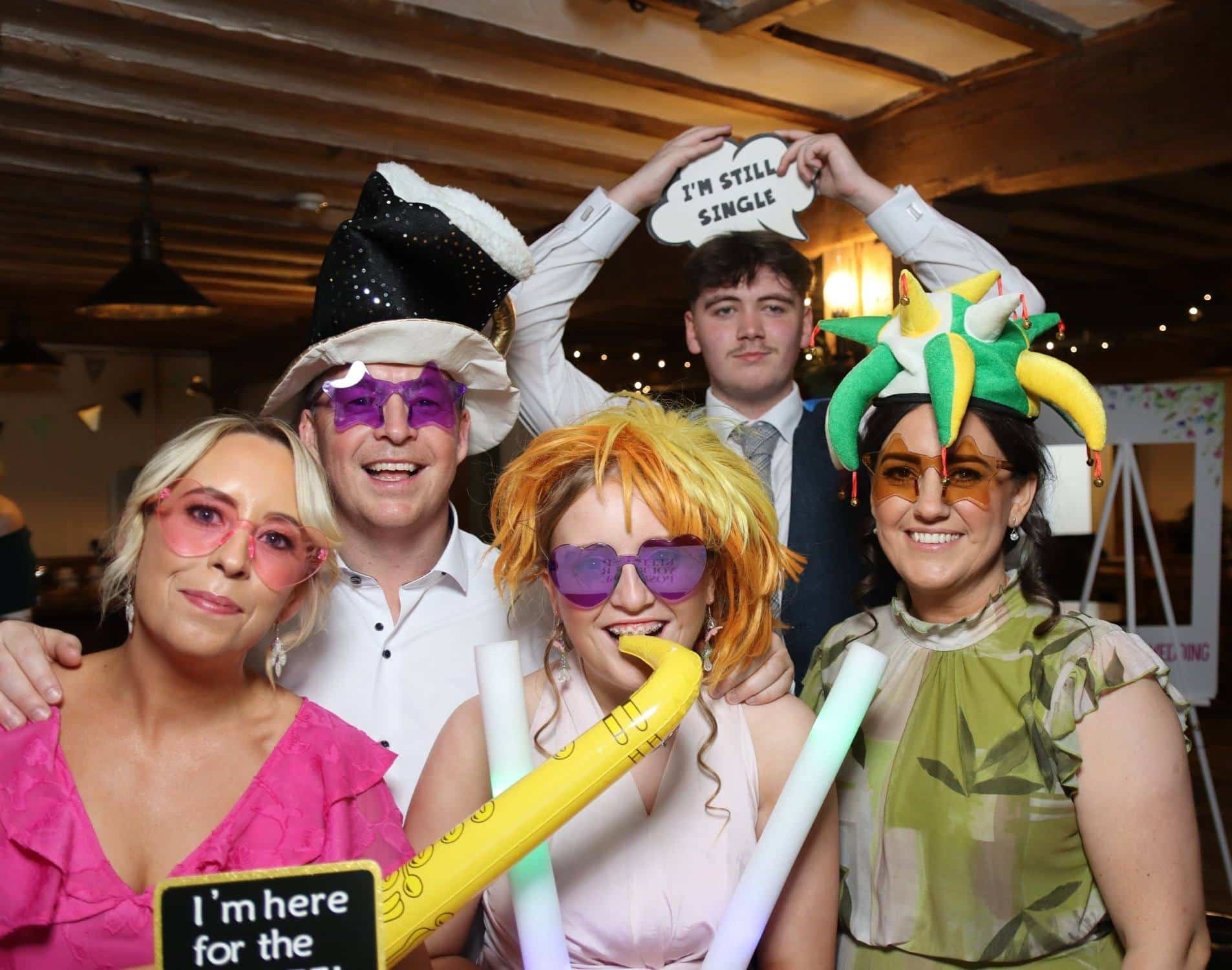 Group of people wearing colorful costumes and props, posing at a party with playful expressions and signs.