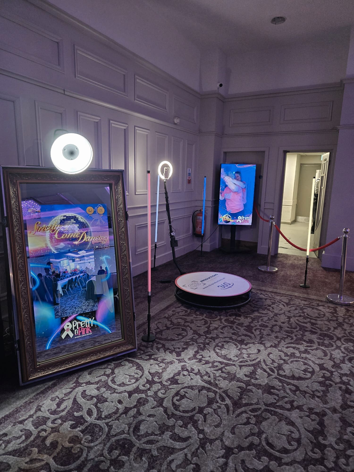 Photo booth setup with mirrors, ring lights, and screens in a well-lit room with decorative carpet.