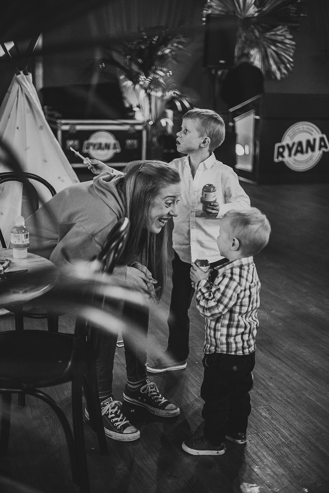 Woman interacting joyfully with two young boys indoors, surrounded by playful decor.