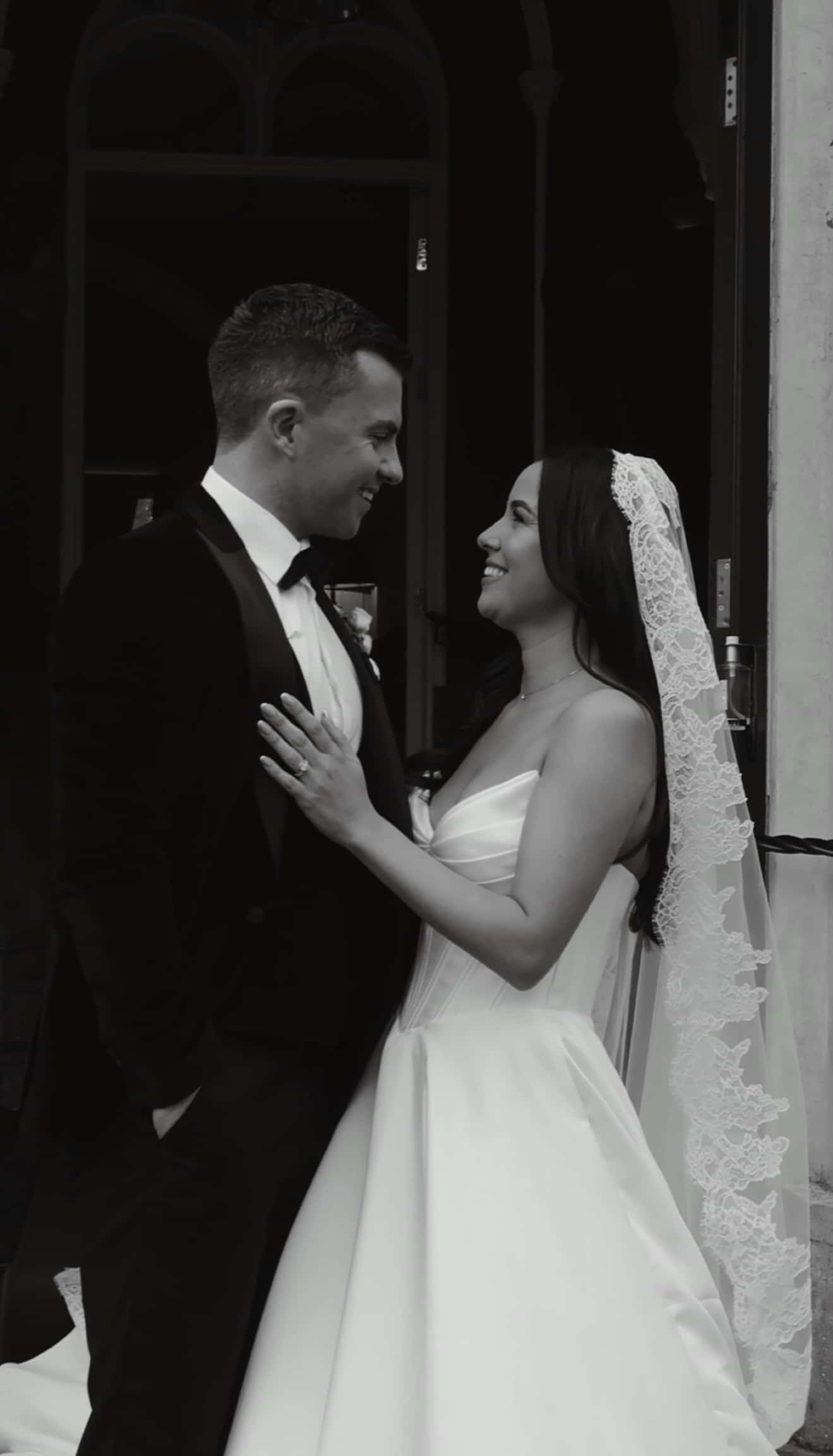 Black and white photo of a bride and groom smiling at each other.