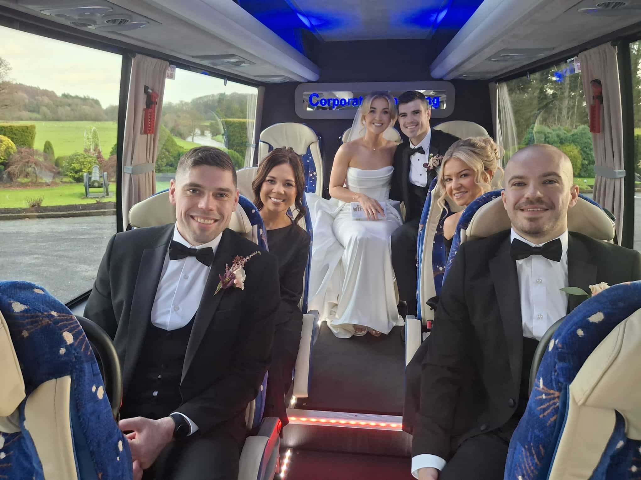 Wedding party smiling inside a limo bus, with bridesmaids and groomsmen in formal attire.