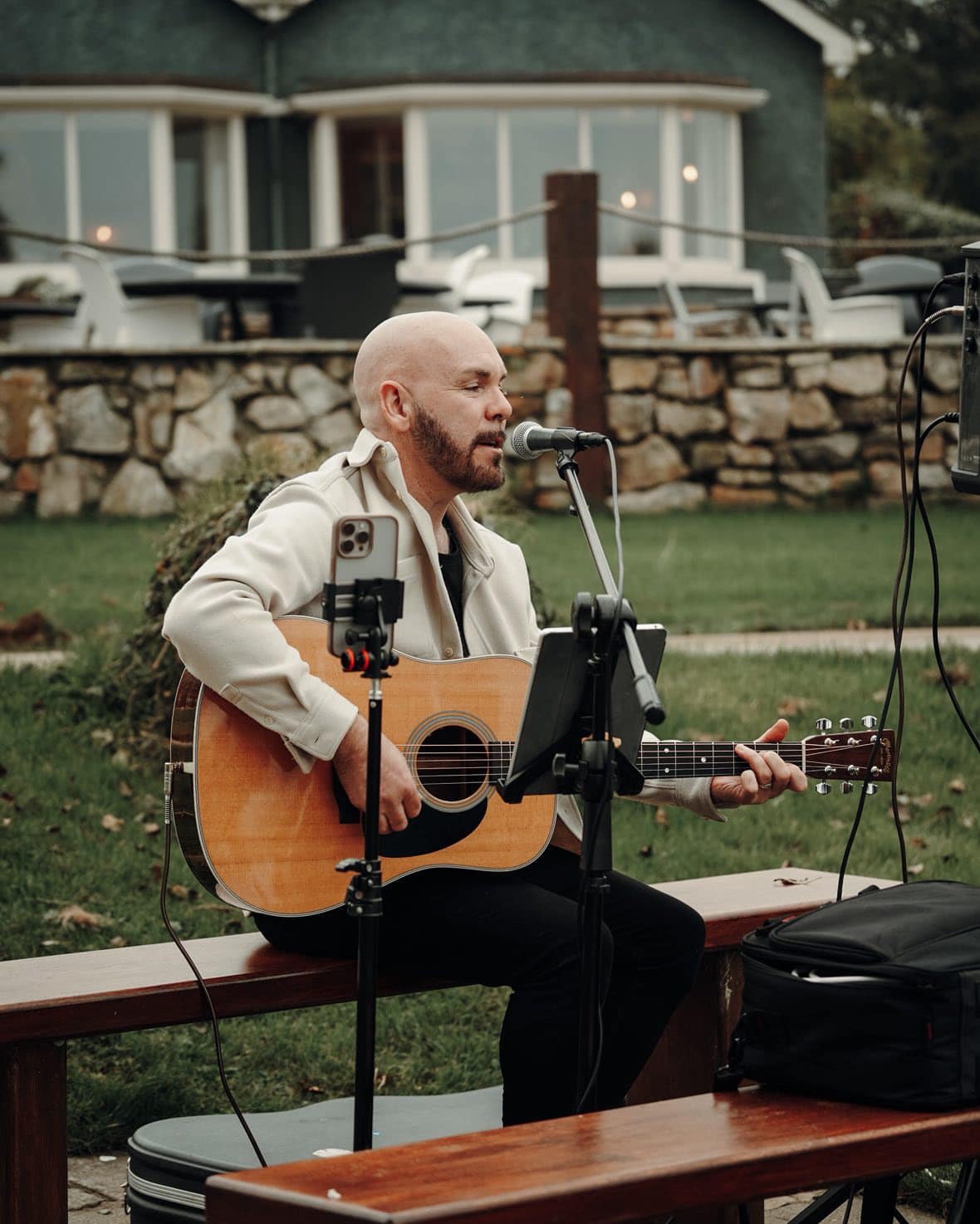 Man playing acoustic guitar and singing outdoors with a microphone setup.
