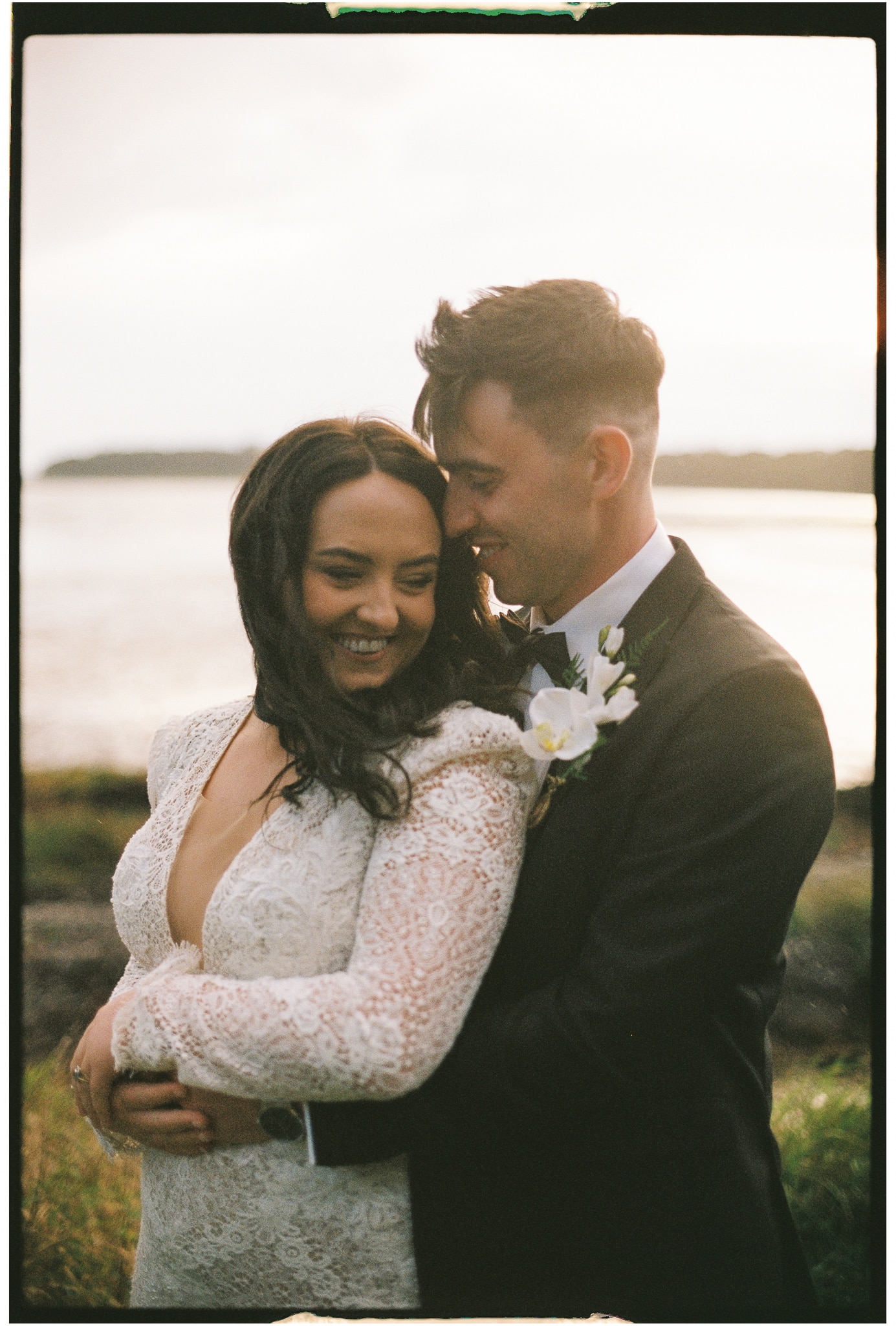 Bride and groom embracing outdoors at sunset, smiling and happy.