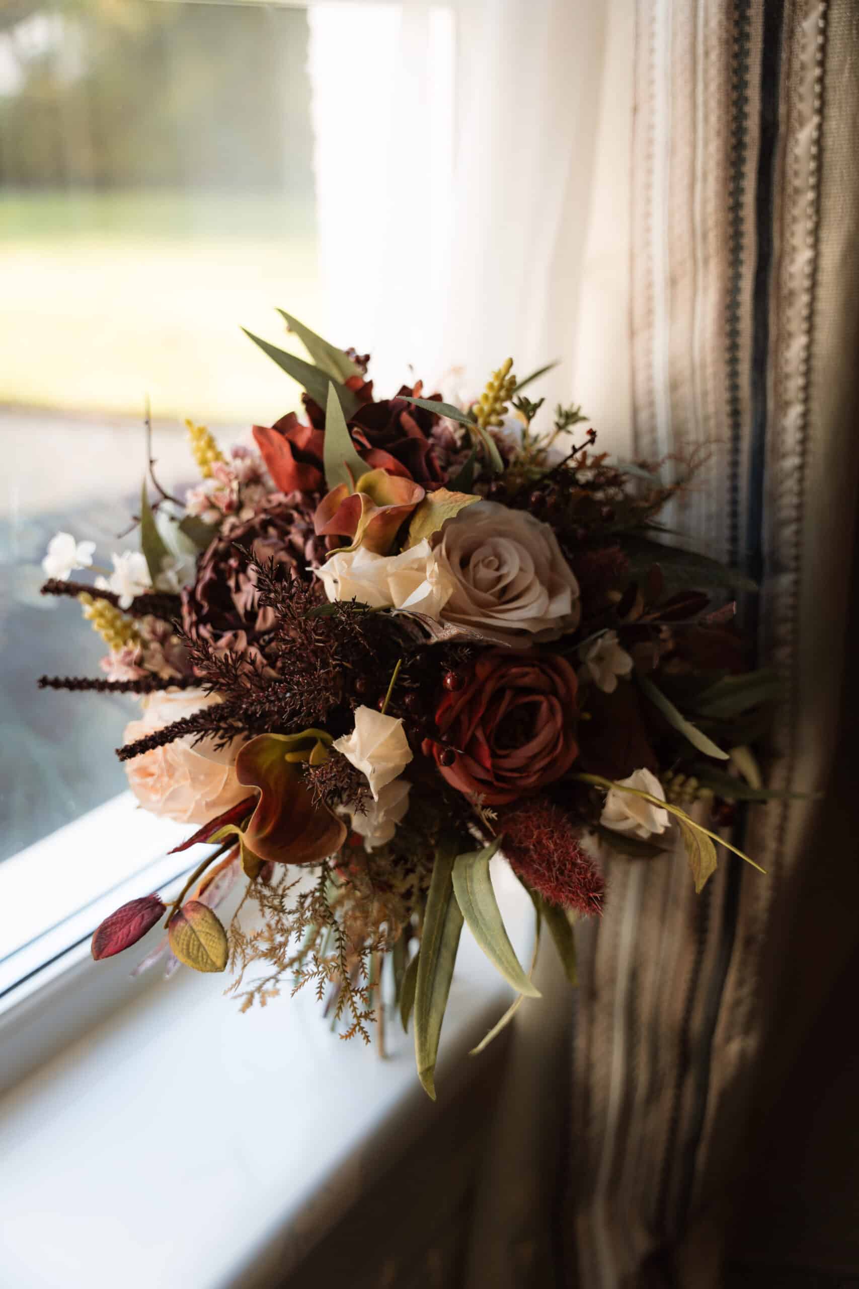 Elegant wedding bouquet with roses and greenery placed on a window sill.