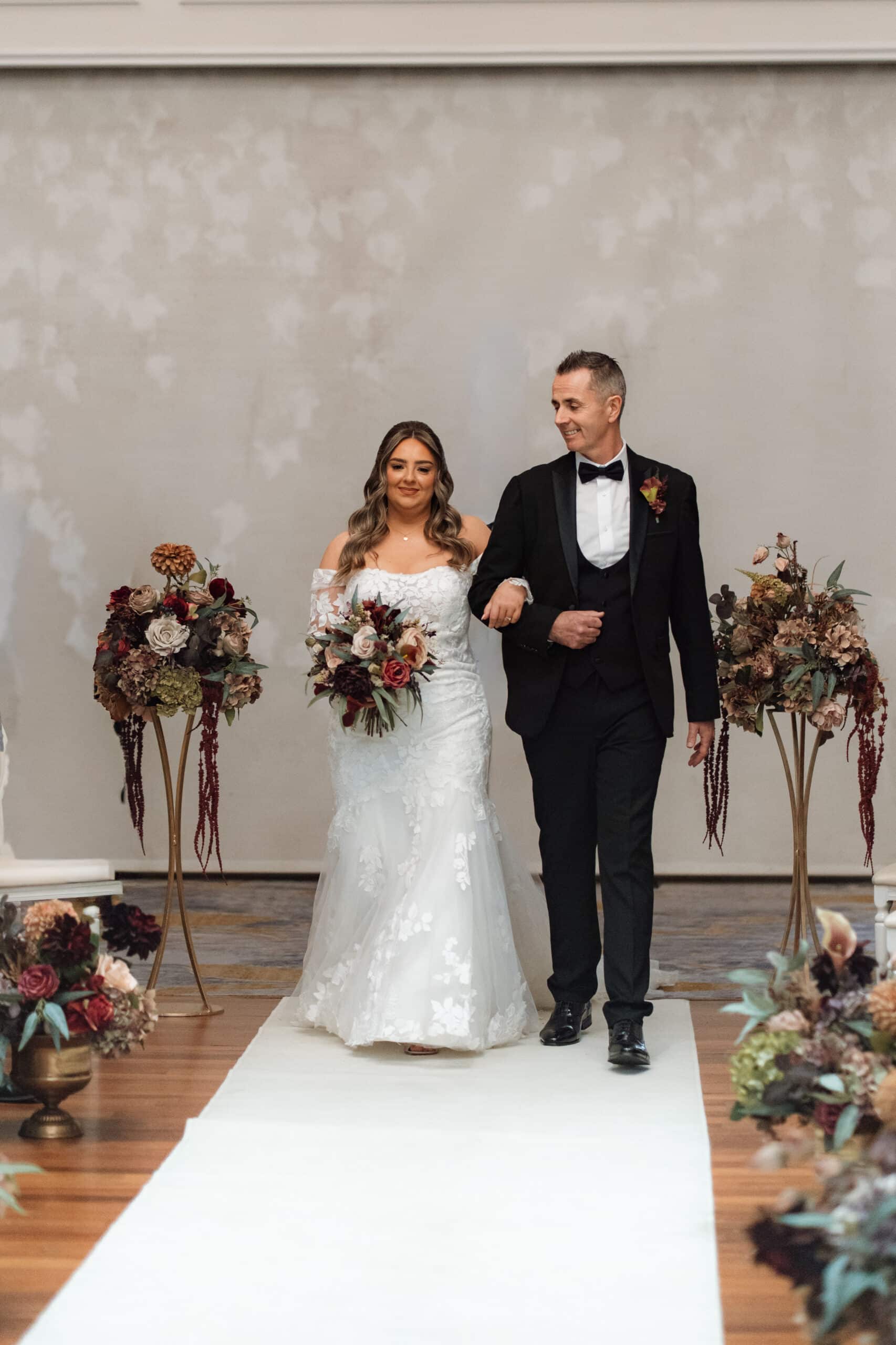 Bride and groom walking down the aisle with floral arrangements.