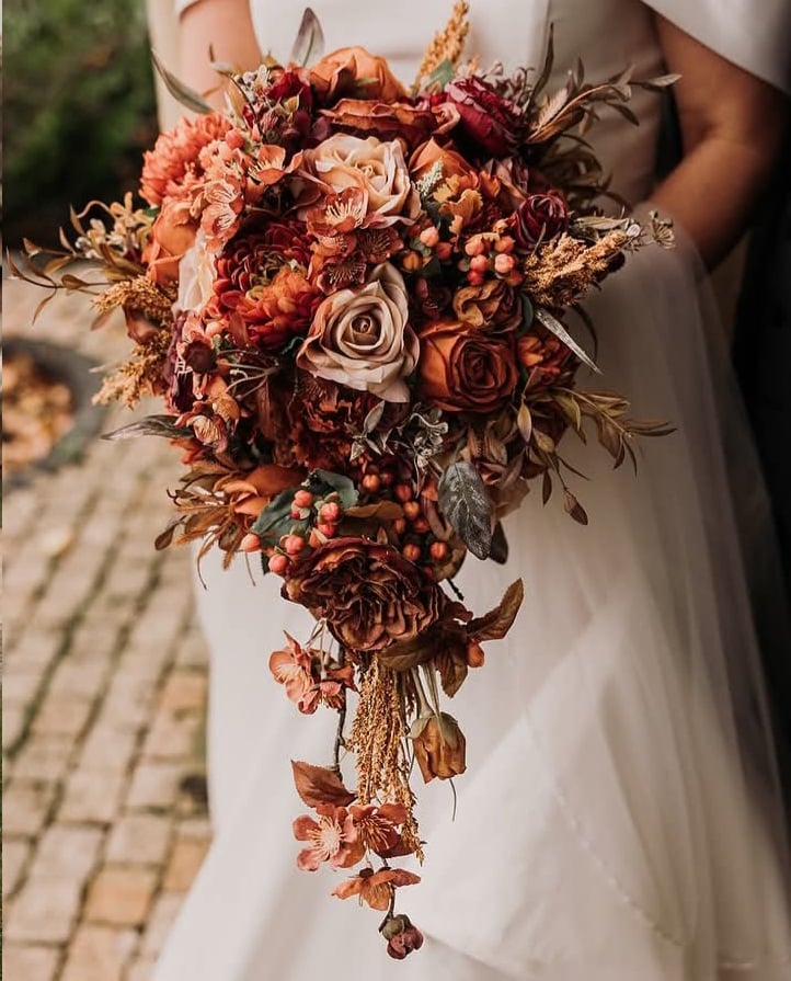 Bride holding cascading bouquet with autumn-colored flowers and foliage.
