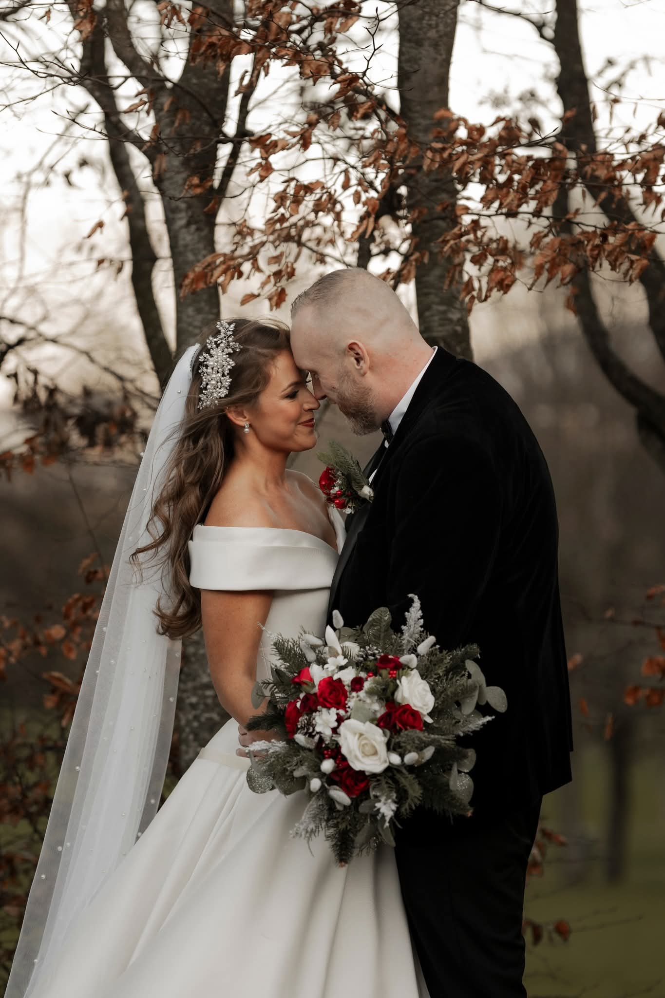 Bride and groom embracing outdoors with a bouquet and autumn backdrop.