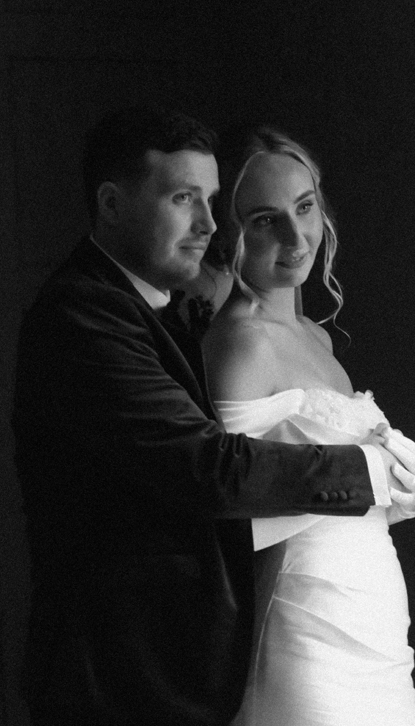 Black and white photo of a bride and groom embracing, smiling softly.