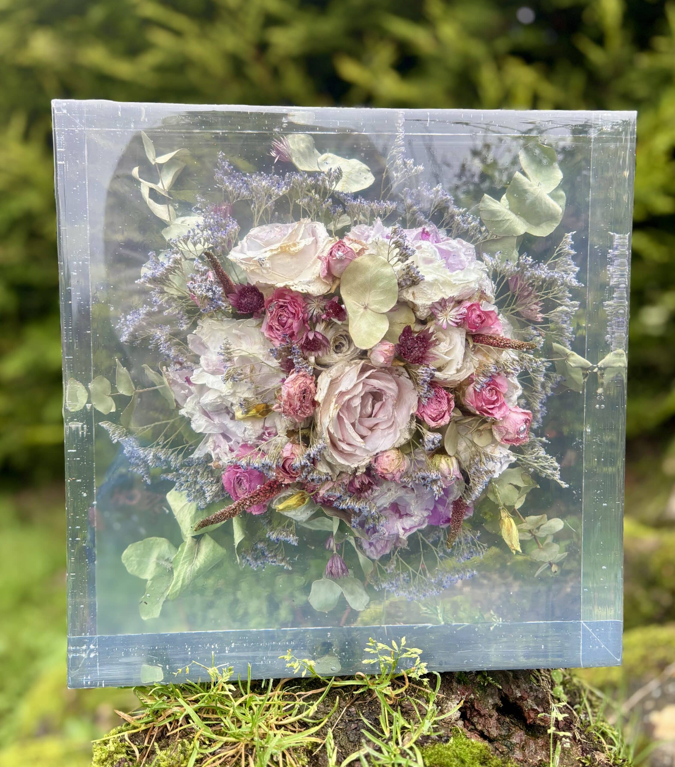 Preserved floral bouquet encased in a clear box, set on a grassy surface.