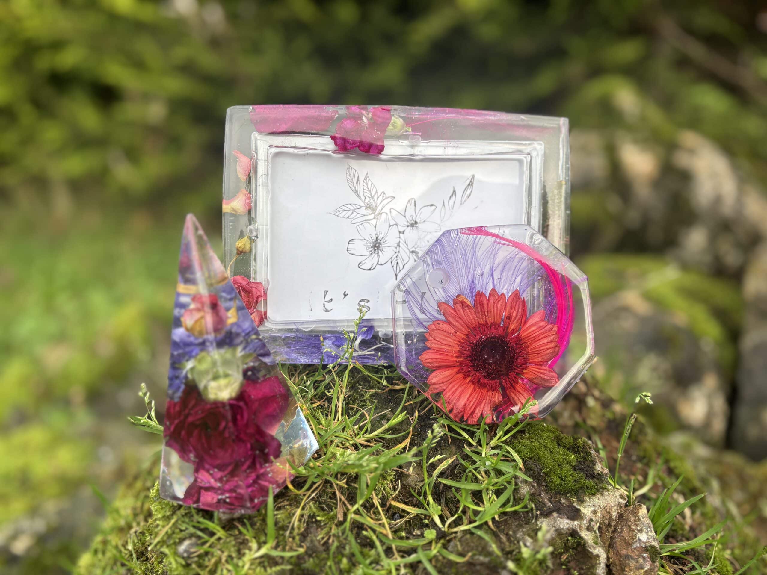 Clear resin art with embedded flowers on grassy rock background.