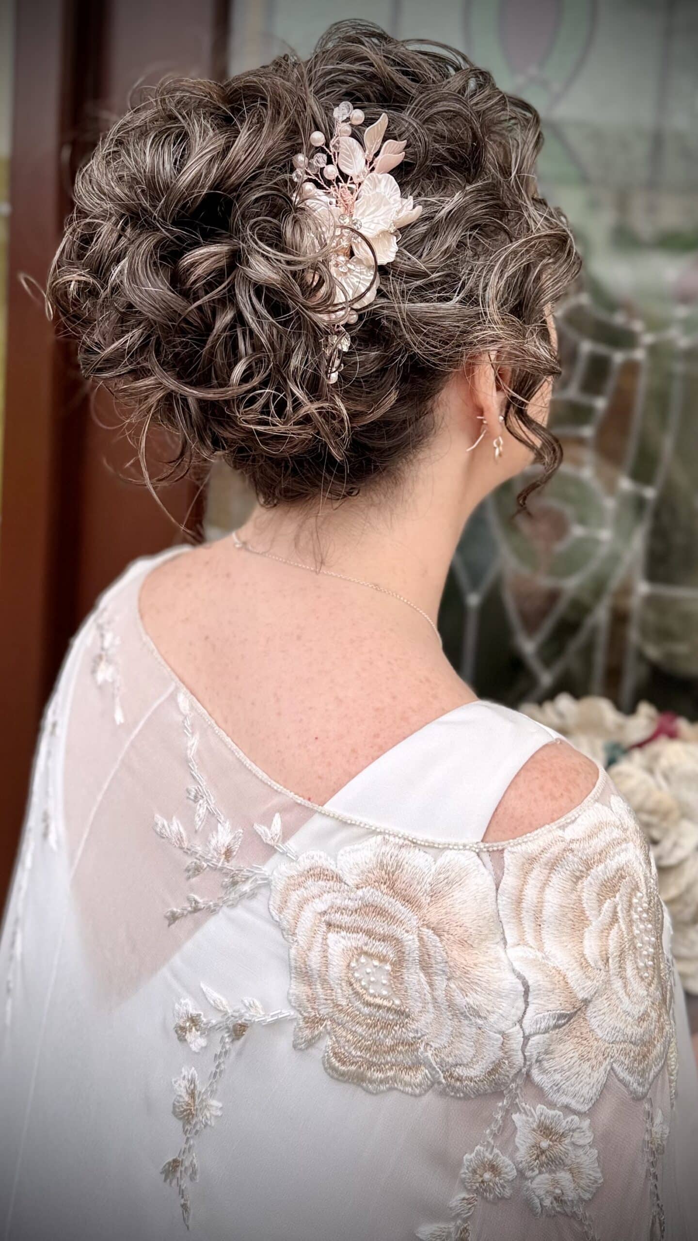 Elegant updo with floral hair accessory, worn by a person in a lace dress.