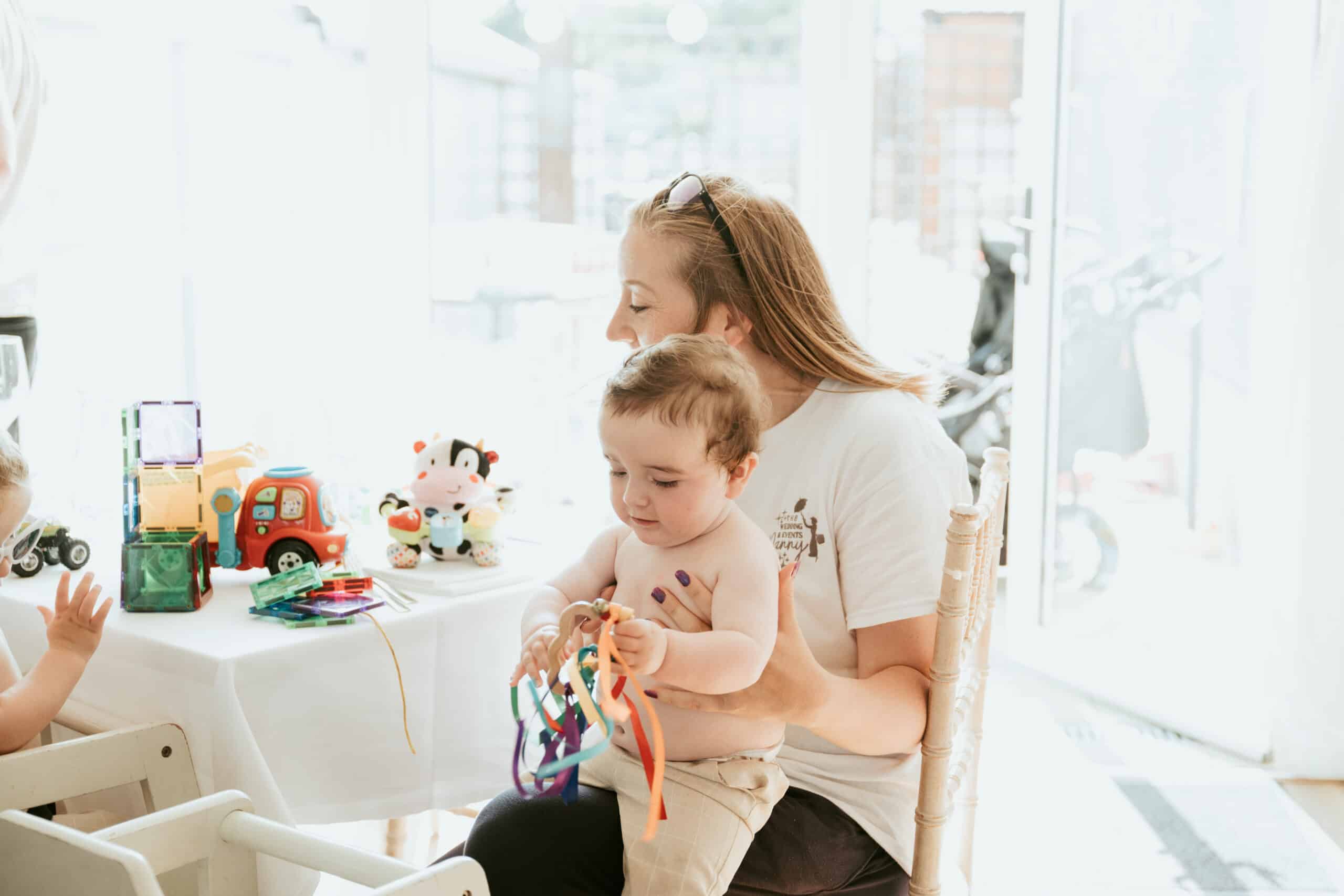 Woman holding a baby with colorful ribbon toys at a table with children's toys.